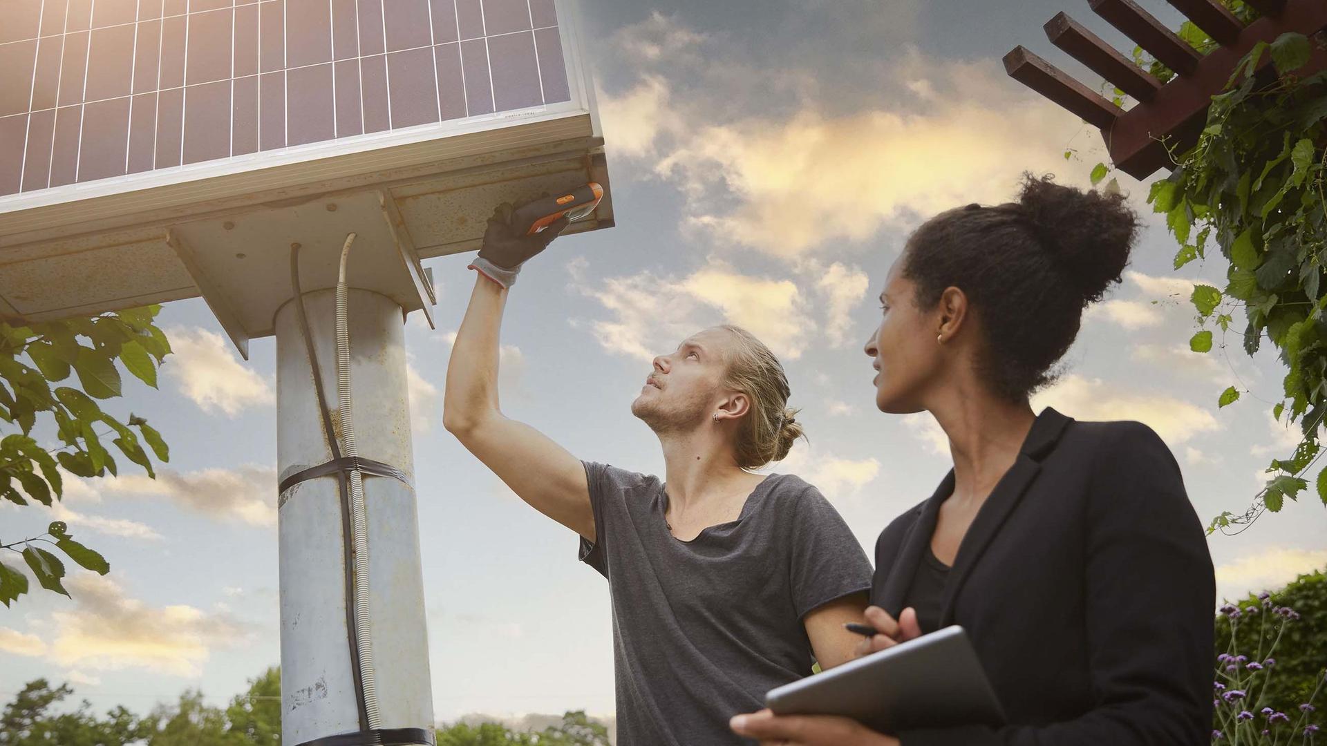 Ein blonder Mann mit Zopf und eine dunklehaarige Frau mit Zopf überprüfen ein Photovoltaik-Panel.