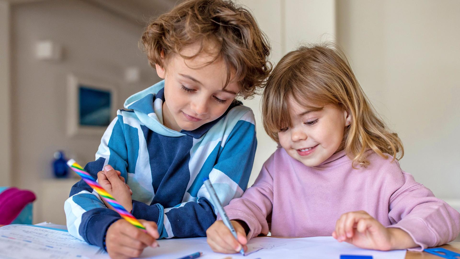 Junge und Mädchen malen mit bunten Stiften auf Papier.