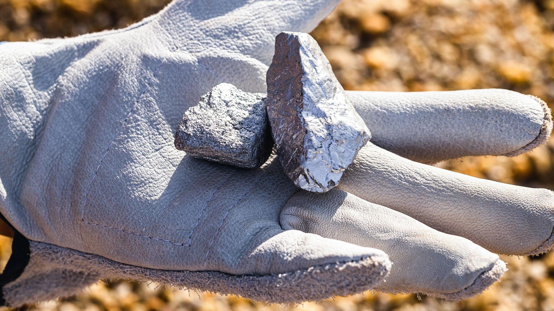 Hand mit einem weißen Handschuh, die Silbersteine und Silbererz hält.