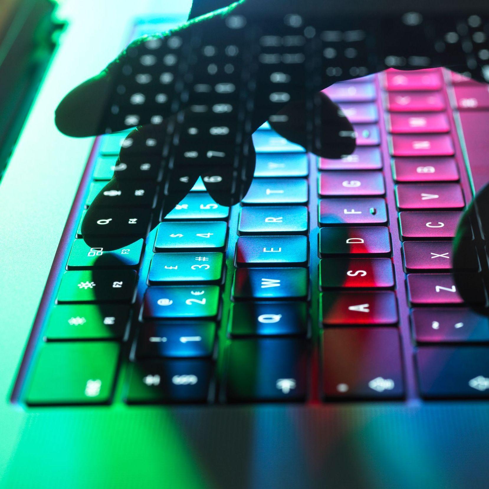Eine Hand tippt auf einer Tastatur, welche in Regenbogenfarben leuchtet.