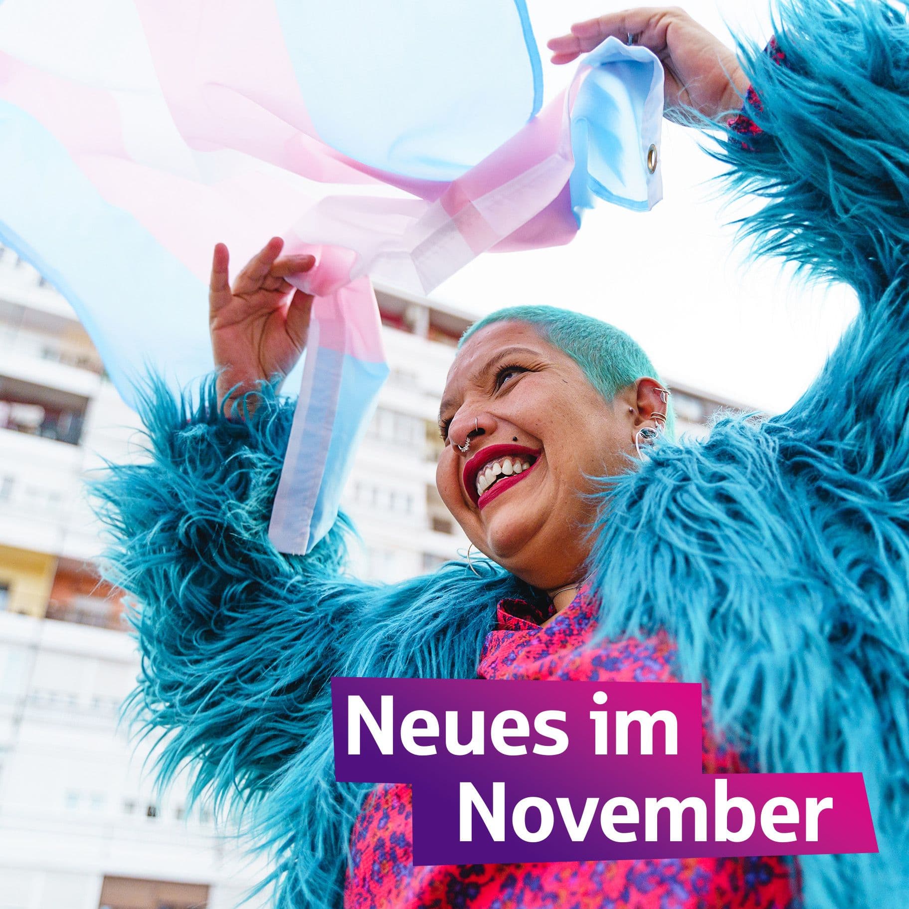 Eine Frau mit flauschiger Jacke und türkisfarbenen Haaren freut sich. Sie schwenkt eine bisexuelle Flagge.