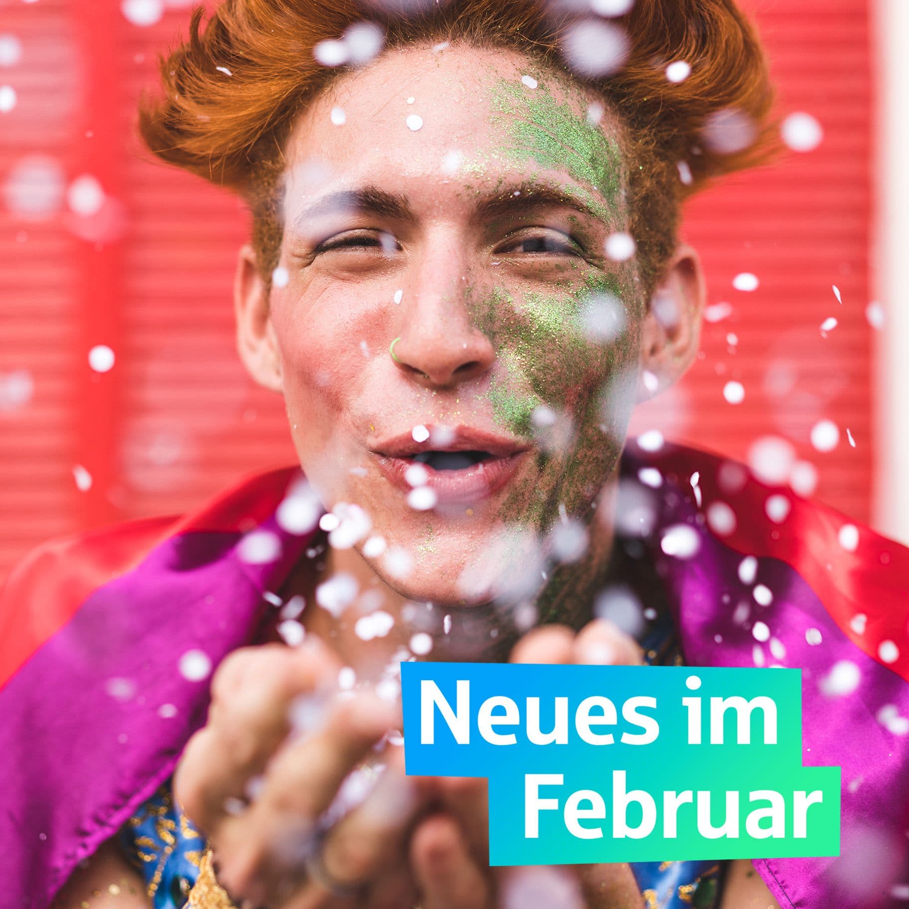 Ein junger Mann mit Schminke im Gesicht pustet Konfetti Richtung Kamera. Auf einer grafischen Fläche steht Neues im Februar.