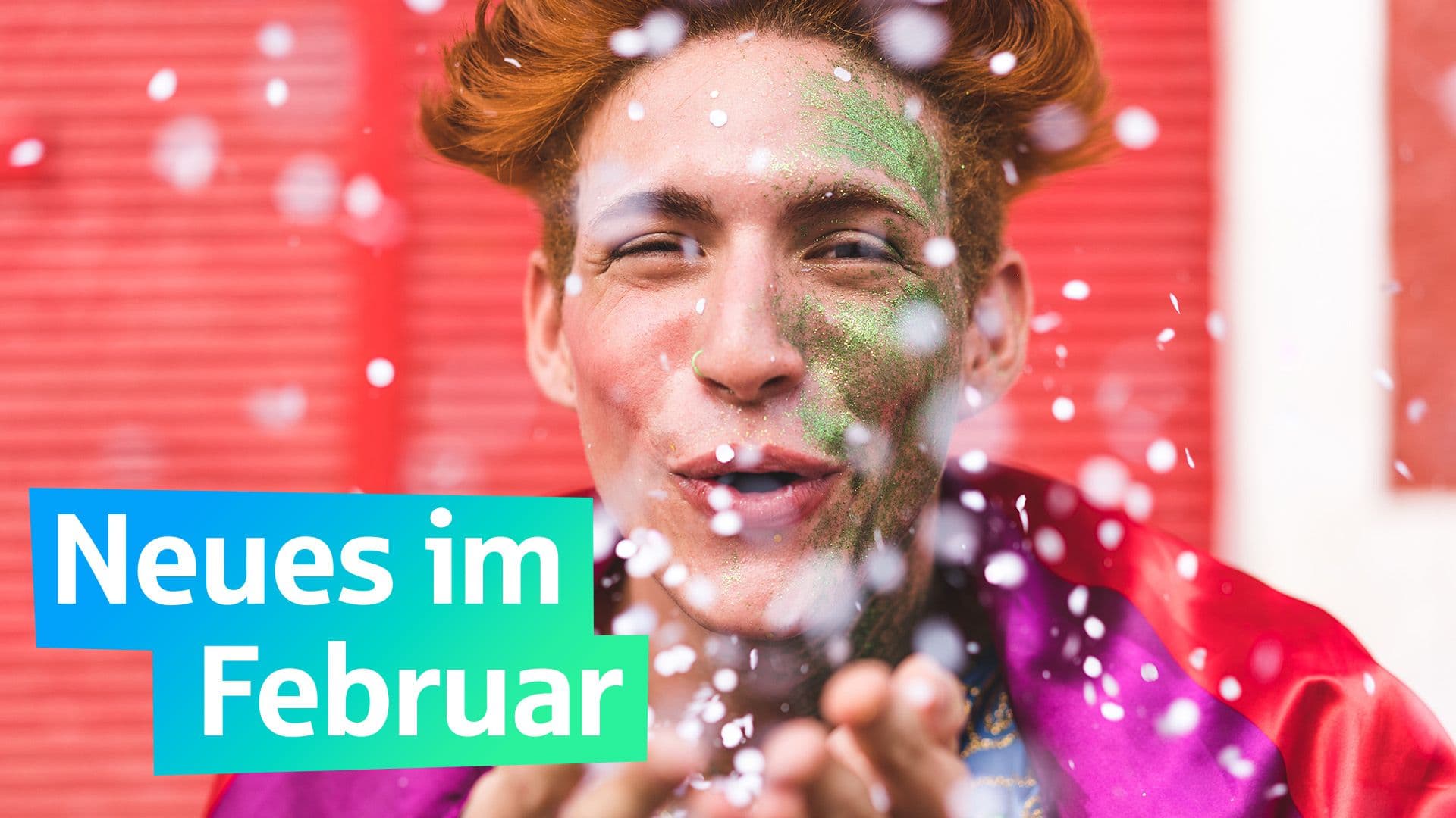 Ein junger Mann mit Schminke im Gesicht pustet Konfetti Richtung Kamera. Auf einer grafischen Fläche steht Neues im Februar.
