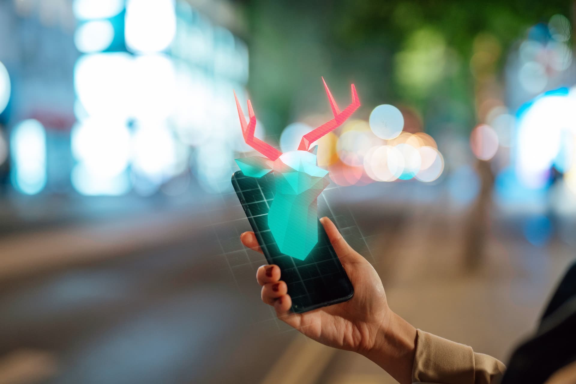 Nahaufnahme einer Person, die einen Handydisplay hochhält. Darauf zu sehen ein digital generiertes 3D-Rentier, das aus dem Smartphone zu kommen scheint.