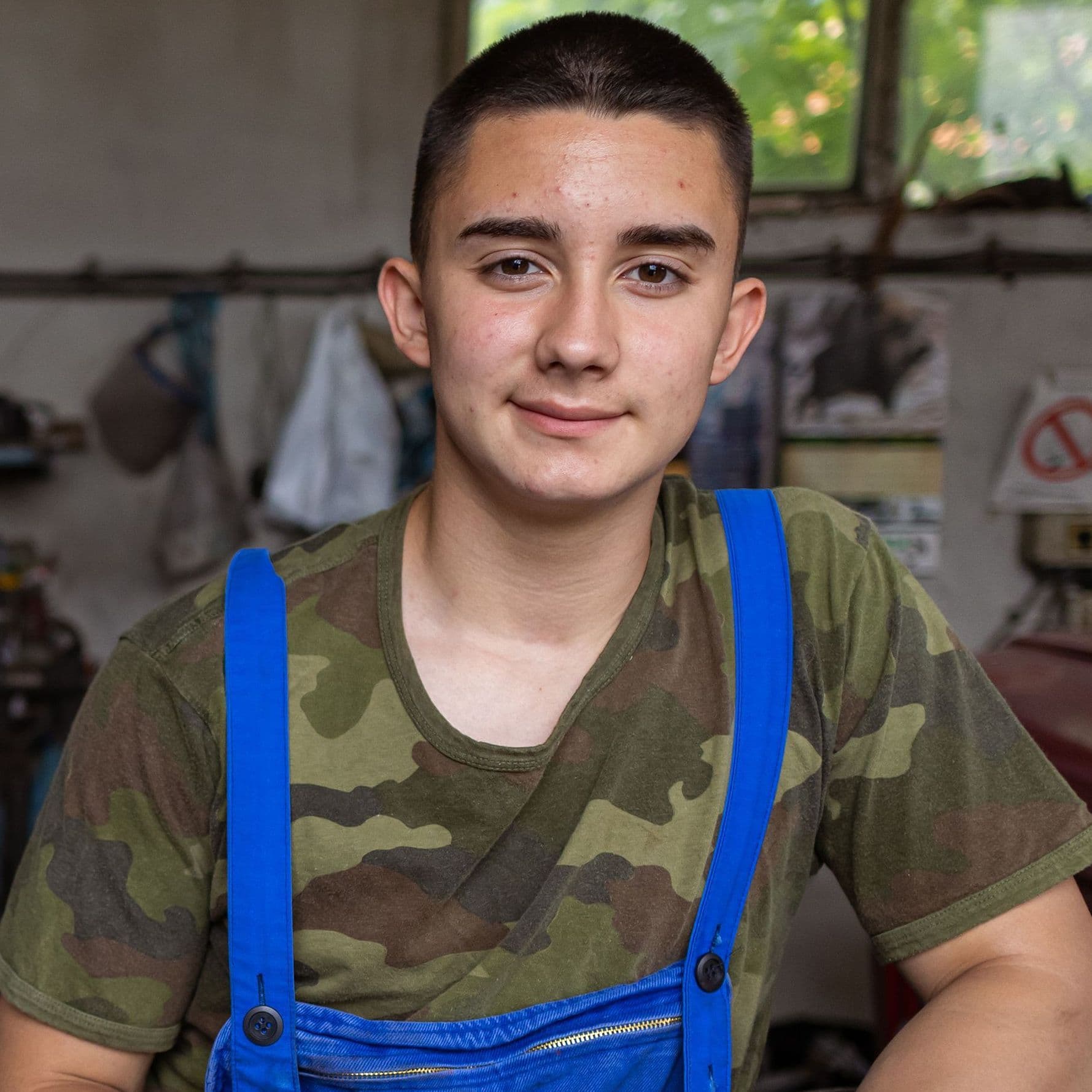 Fachkräftemangel Ein junger Mann in Camouflage T-Shirt und Blaumann sitzt in einer Werkstatt