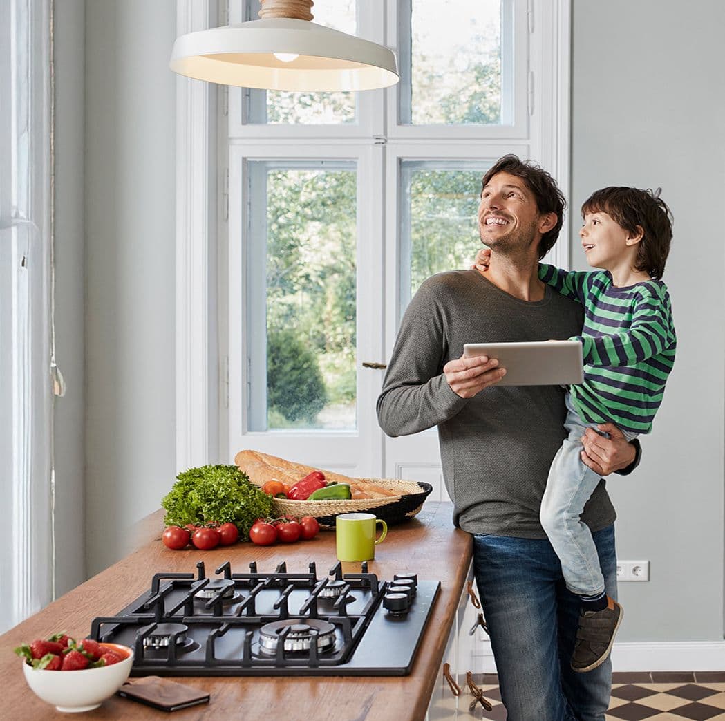 Vater hält Kind im Arm in moderner Küche mit Tablet in der Hand