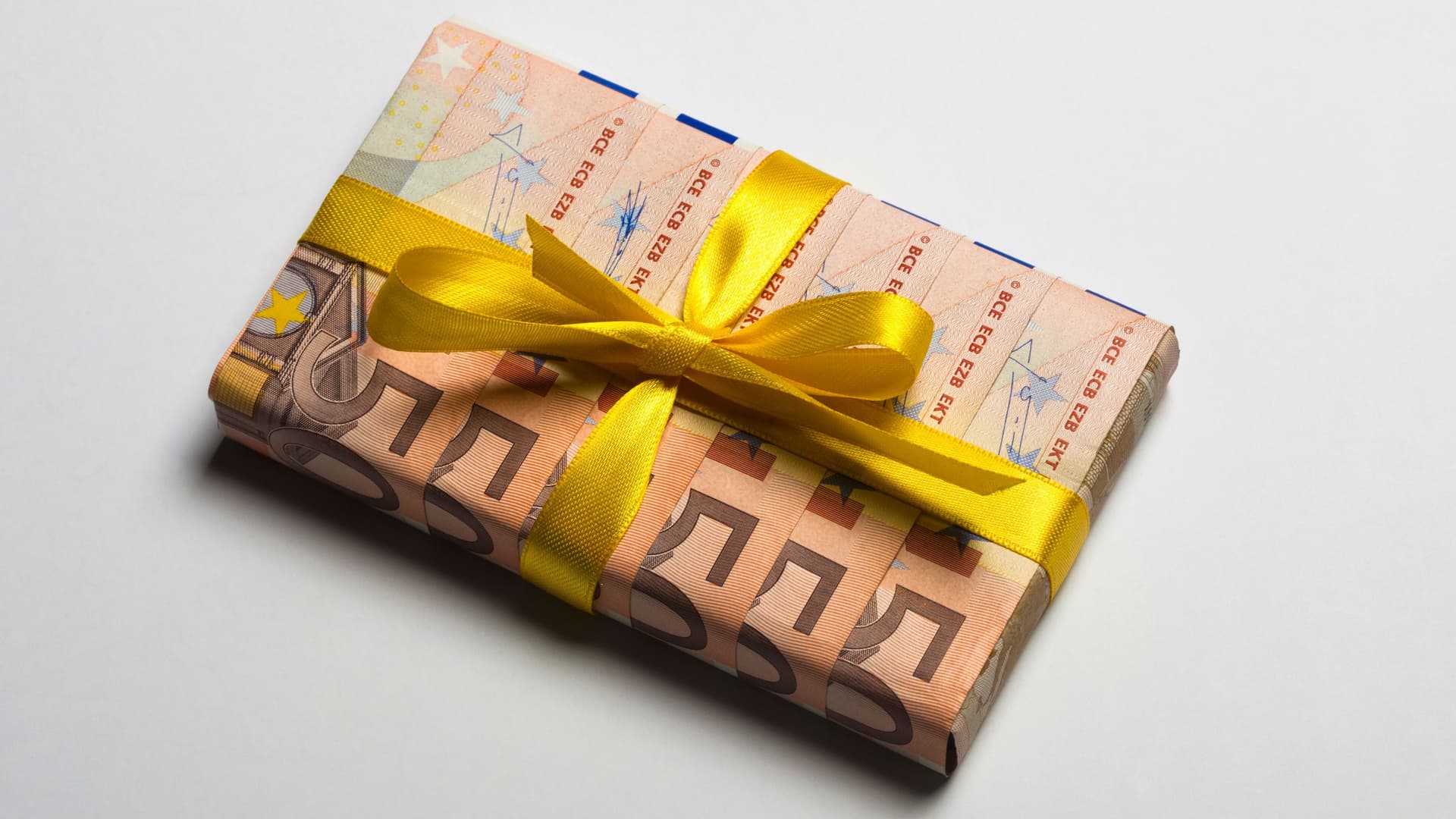 Fünfzig Euro-Geldscheine, die gefaltet wurden, um ein Geschenk damit zu verpacken. Darum ist eine gelbe Schleife aus Geschenkband.