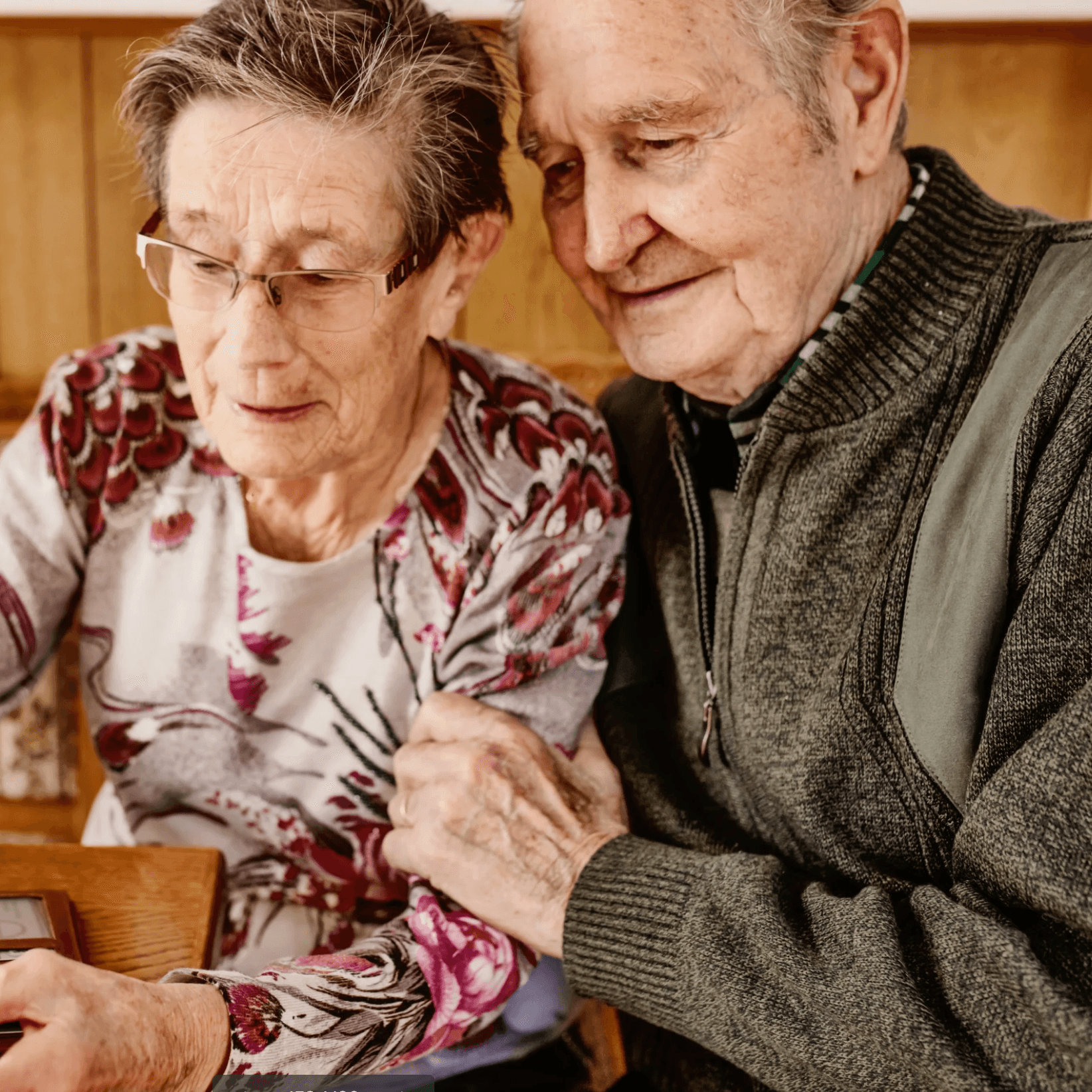 Eine ältere Frau mit Brille hält Banknoten in der Hand, während ein älterer Mann lächelnd über ihre Schulter schaut. Ihre Hände sind verschränkt.