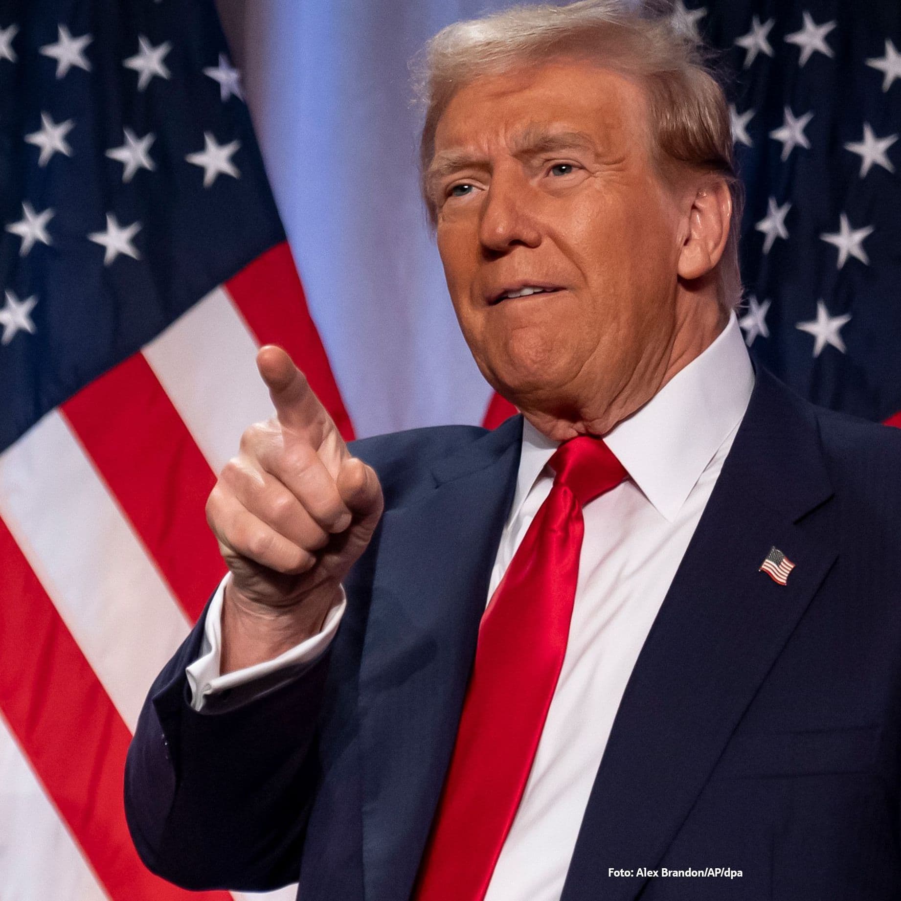 Donald Trump steht vor amerikanischen Flaggen. Er zeigt mit dem Finger Richtung Kamera.