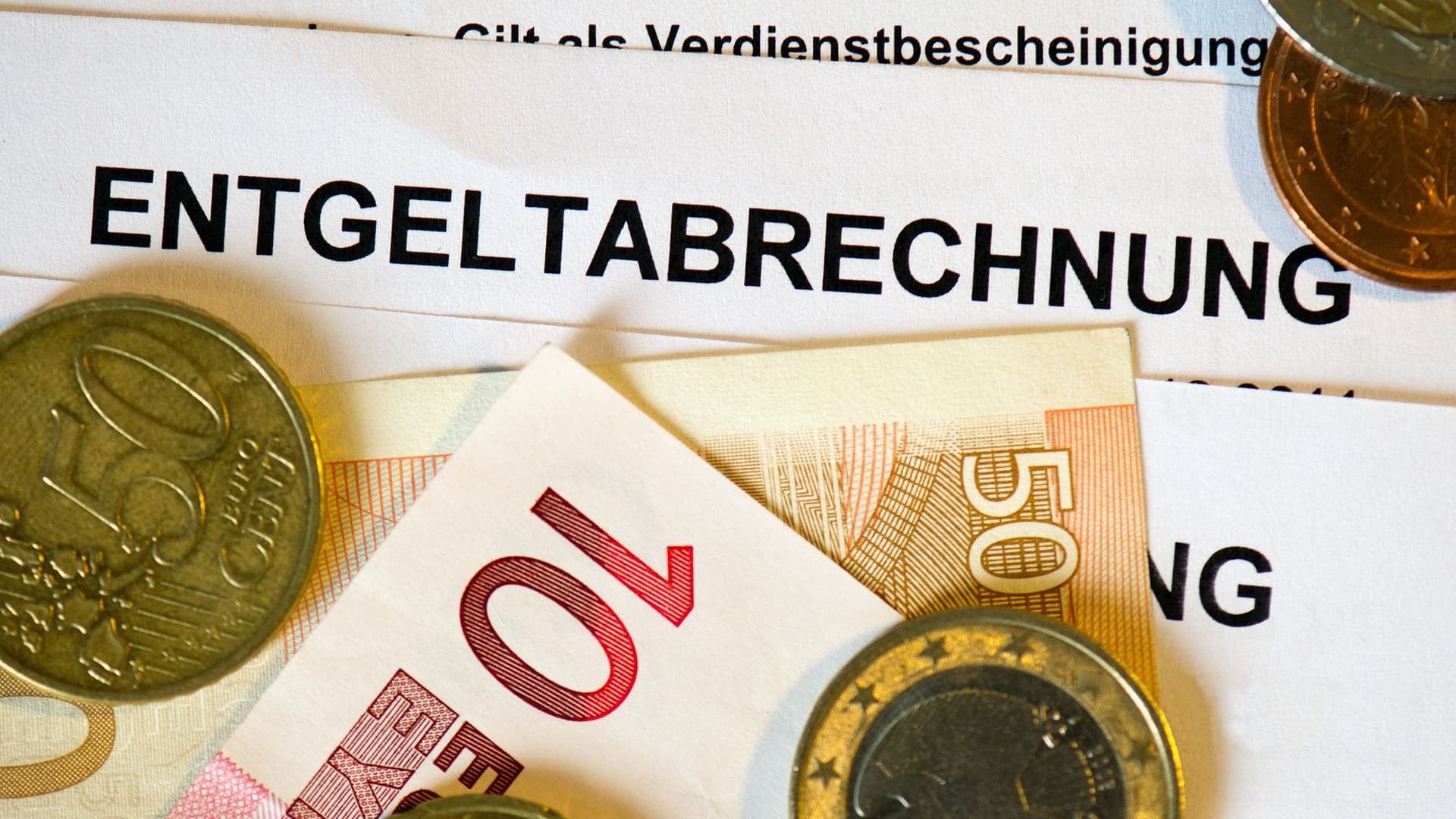 Gehaltsabrechnung mit einigen Münzen und Geldscheinen darauf