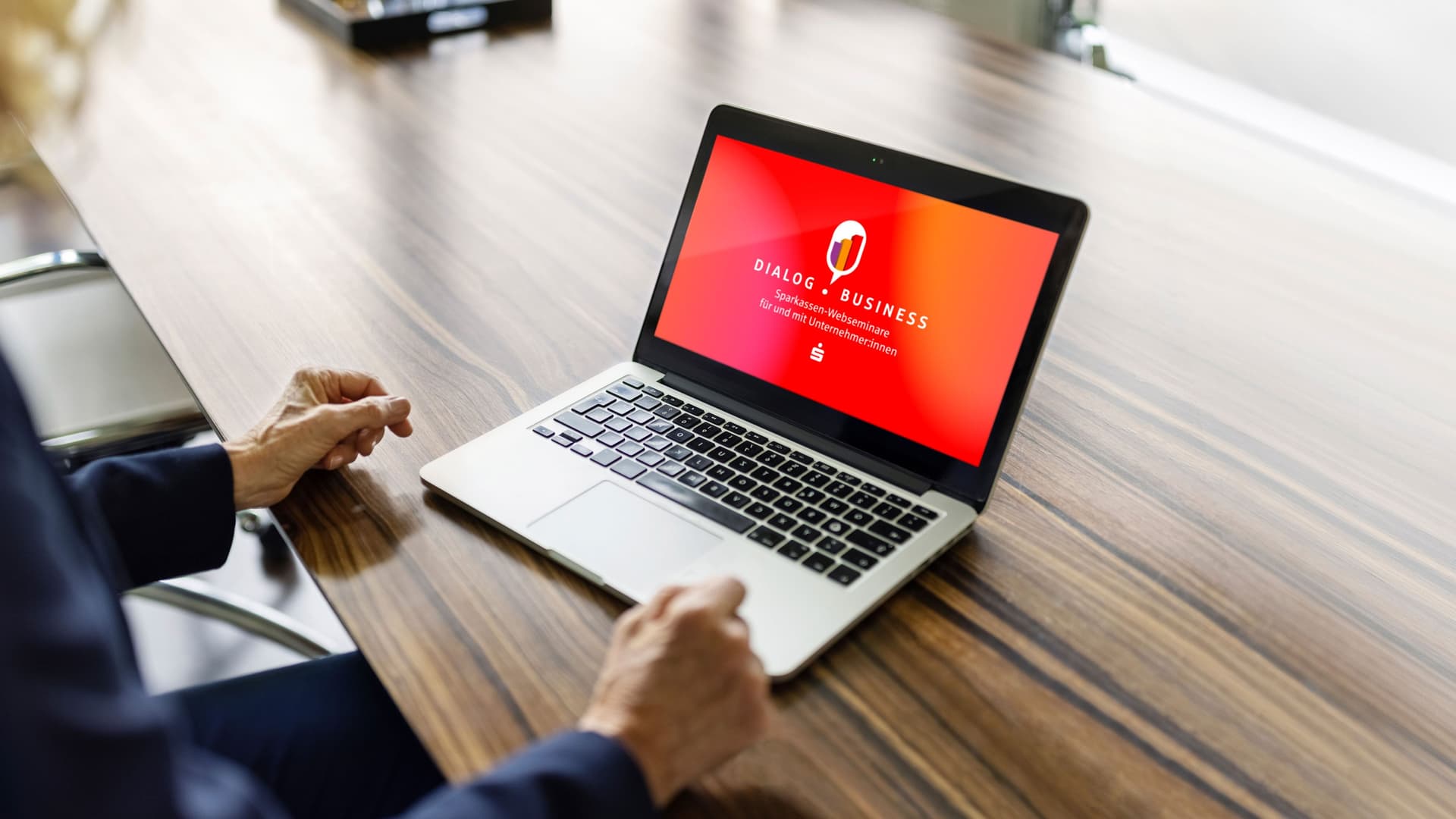 Eine Frau sitzt vor ihrem Laptop.Der Bildschirm ist orange mit Logo DialogBusiness.
