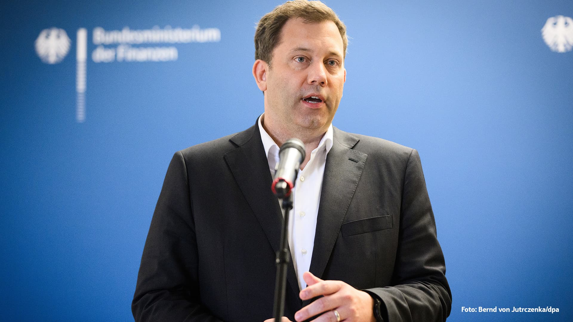 Lars Klingbeil steht in dunklem Anzug und weißem Hemd vor einem Mikrofon, im Hintergrund ist eine blaue Wand. Er wirkt konzentriert und engagiert, während er eine öffentliche Erklärung abgibt.