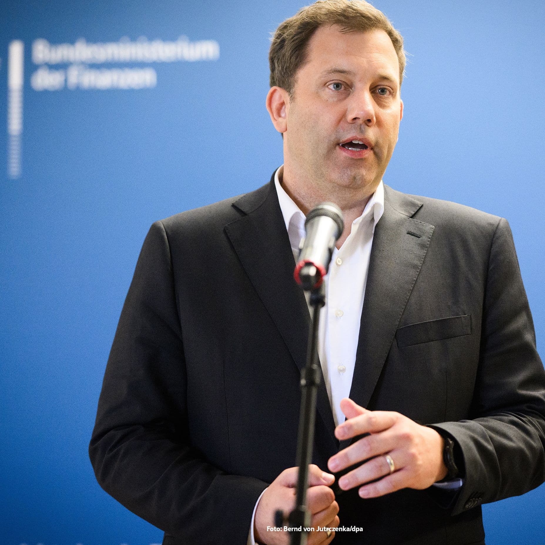 Lars Klingbeil steht in dunklem Anzug und weißem Hemd vor einem Mikrofon, im Hintergrund ist eine blaue Wand. Er wirkt konzentriert und engagiert, während er eine öffentliche Erklärung abgibt.