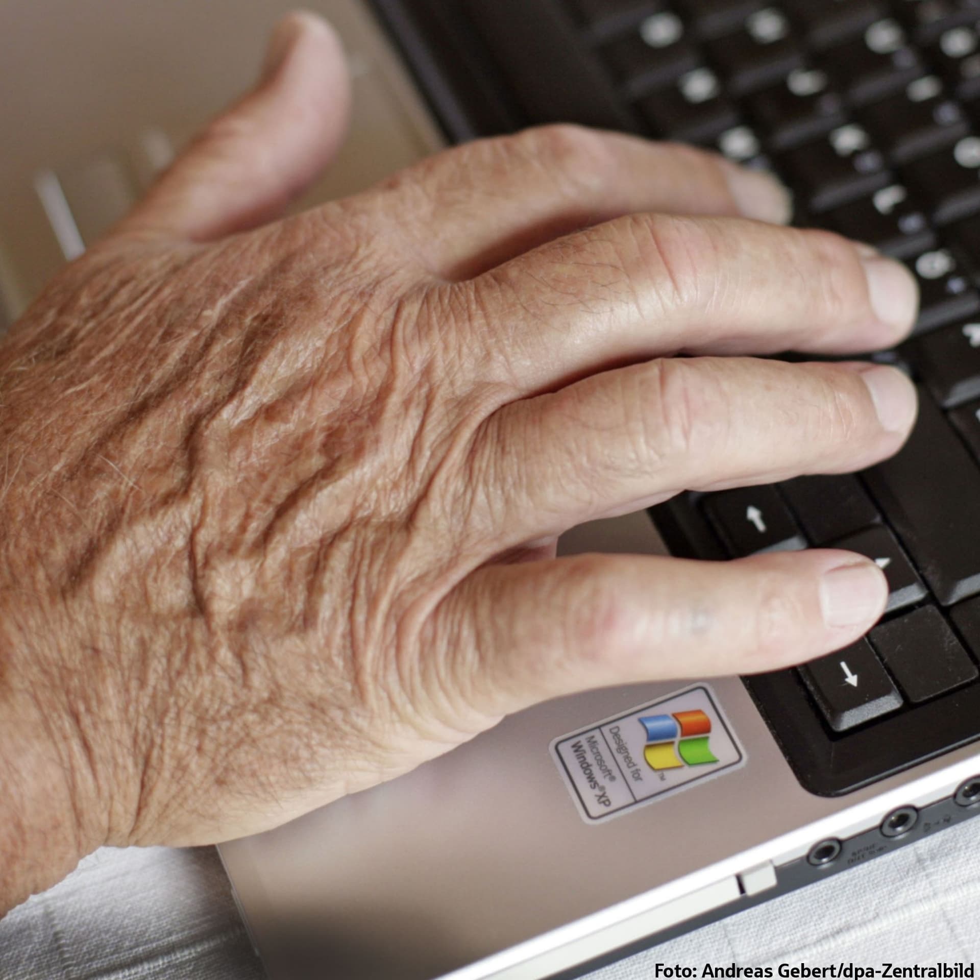 Hand einer älteren Person auf Laptop-Tastatur