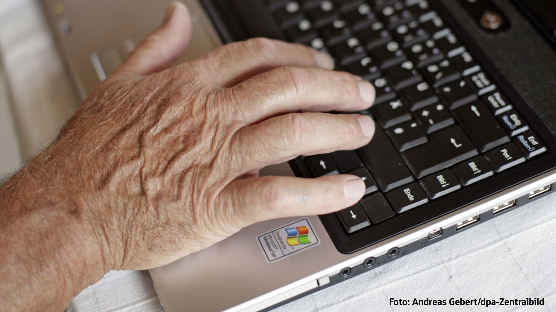 Hand einer älteren Person auf Laptop tastatur