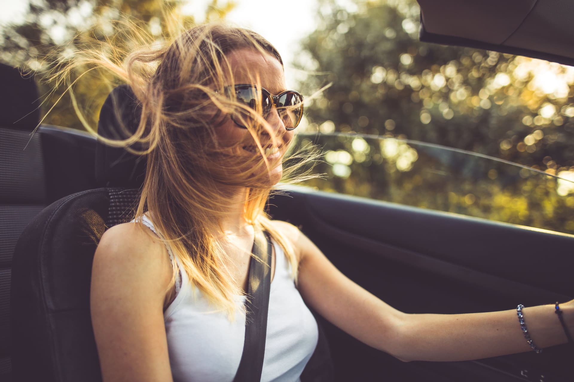 Eine junge, blonde Frau fährt mit wehendem Haar und Sonnenbrille Cabrio.