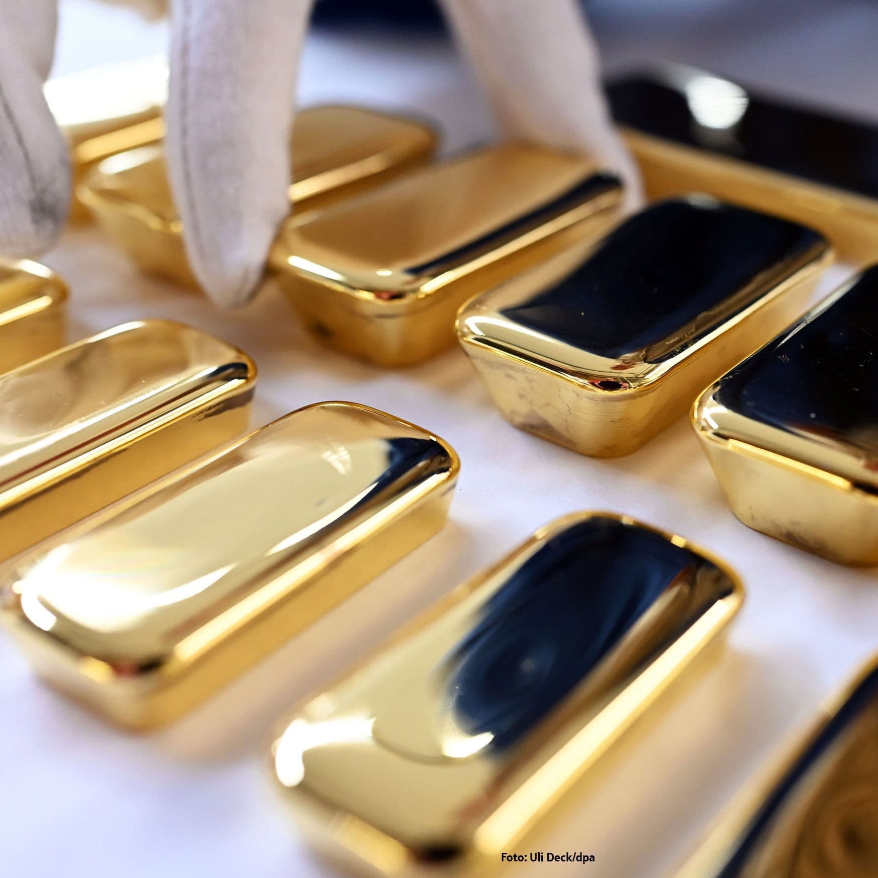 Eine Hand mit einem weißen Baumwollhandschuh sortiert Goldbarren.