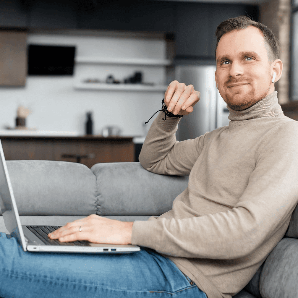 Ein Mann sitzt mit seinem Laptop auf dem Sofa.
