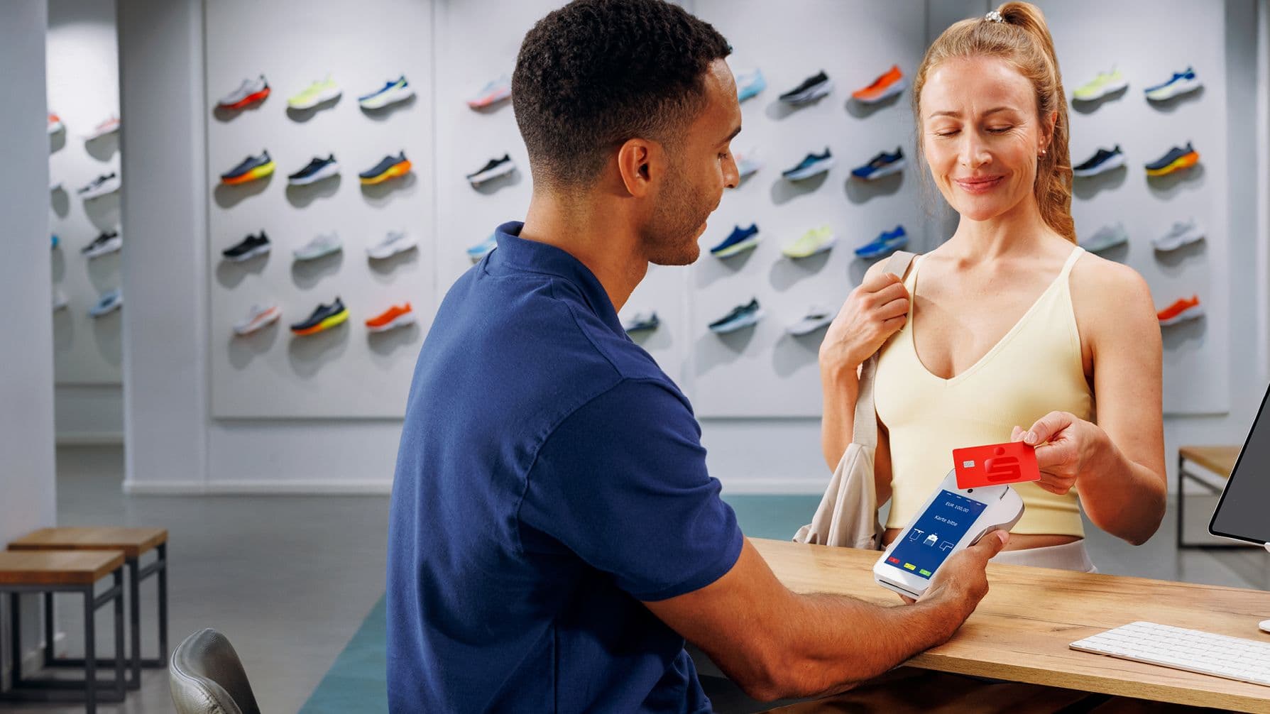 Frau bezahlt mit einer roten Sparkasse Karte an einem Kartenlesegerät in einem Schuhgeschäft.
