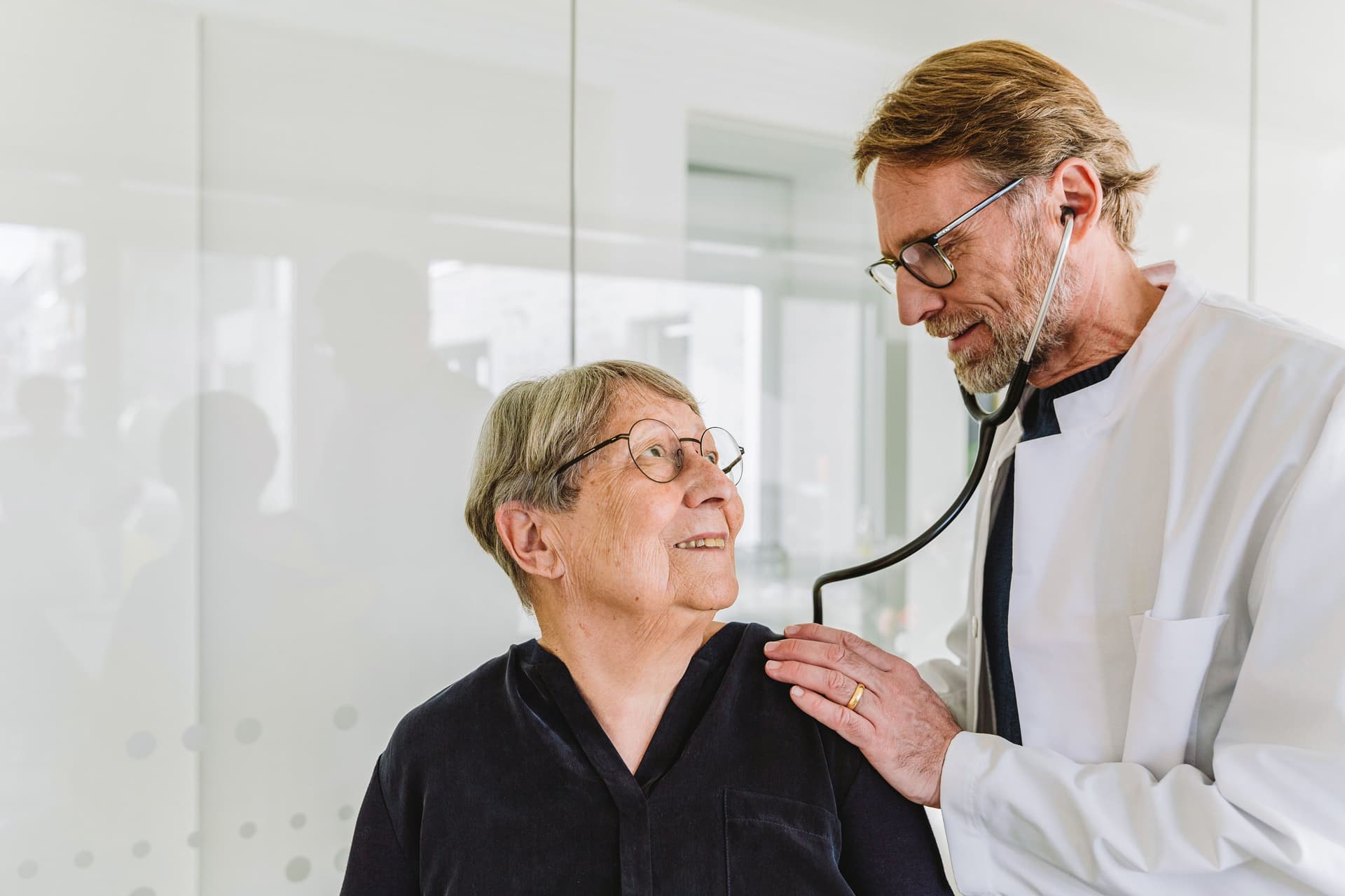 Ein Arzt untersucht eine ältere Patientin mit einem Stethoskop.