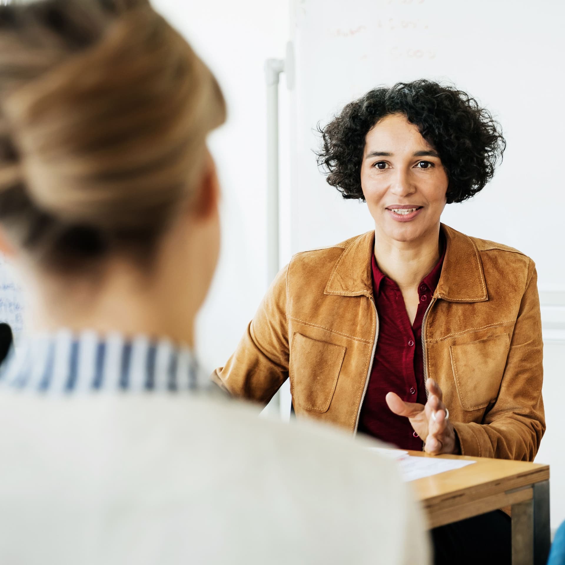 Sitution einer Gehaltsverhandlung: Drei Frauen sitzen an einem Tisch in einem hellen Raum und reden miteinander.