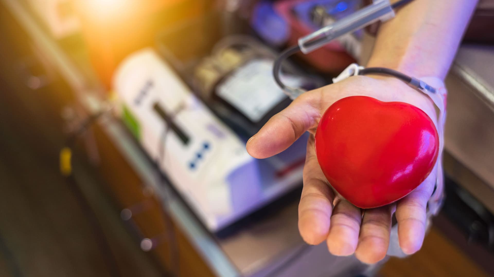 Eine Hand hält ein Herz während einer Bluttransfusion erfolgt.