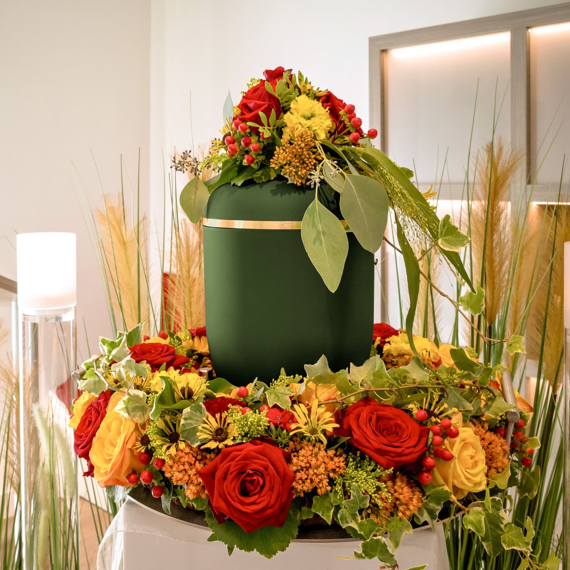 Eine blumengeschmueckte Urne steht aufgebahrt auf einem Sarg