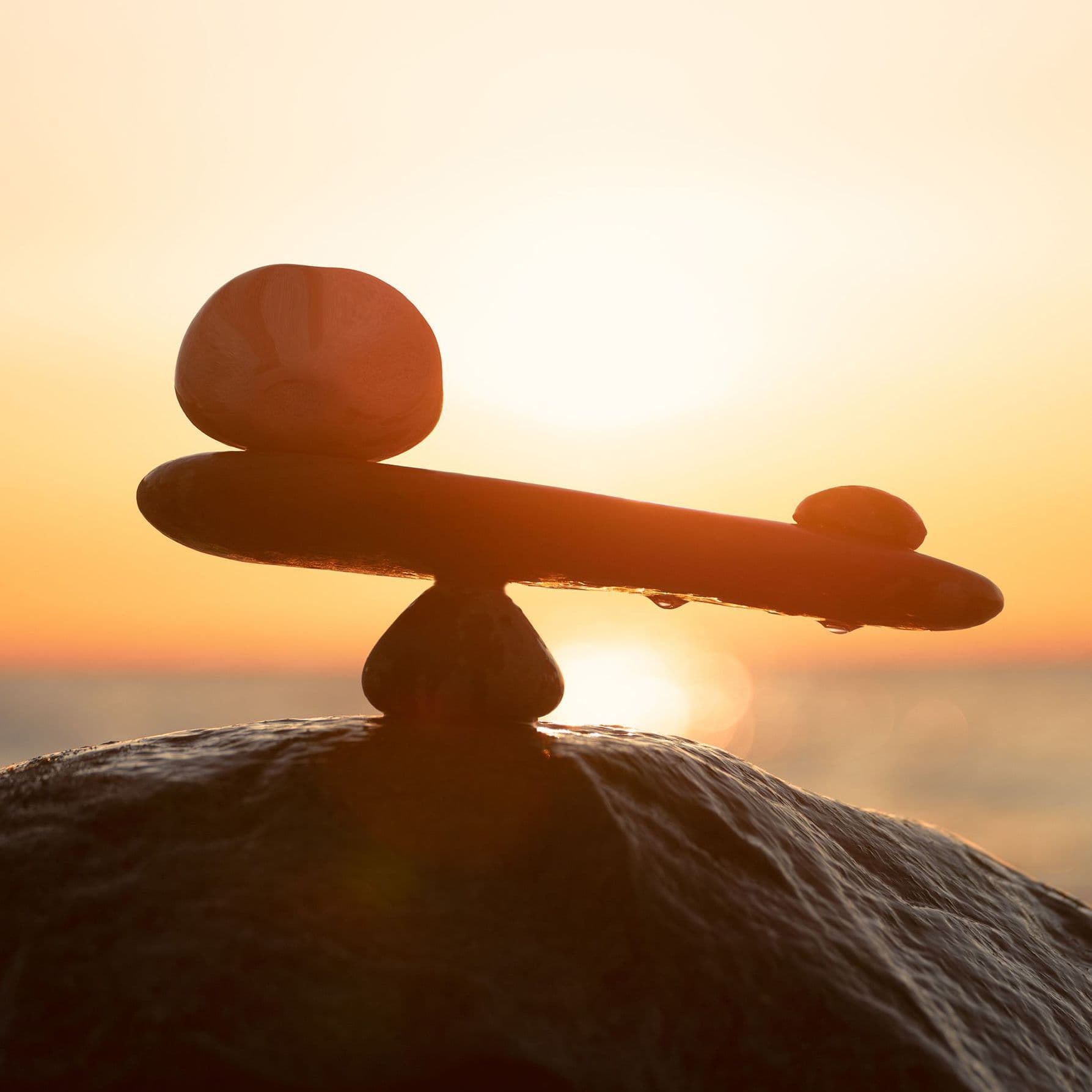 Auf dem Bild sind mehrere Steine ​​zu sehen, die in einer Balance angeordnet sind. Im Hintergrund geht die Sonne unter, und das warme Licht erzeugt eine ruhige, natürliche Stimmung.