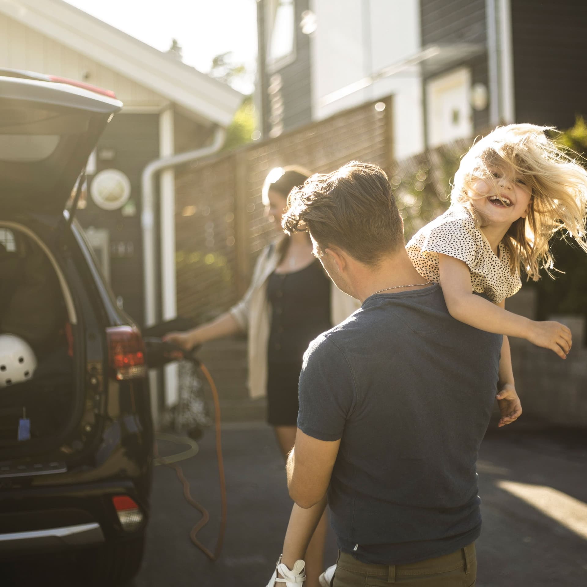 Mutter lädt Elektroauto auf wahrend der Vater und das Kind in der Einfahrt ausgelassen sind.