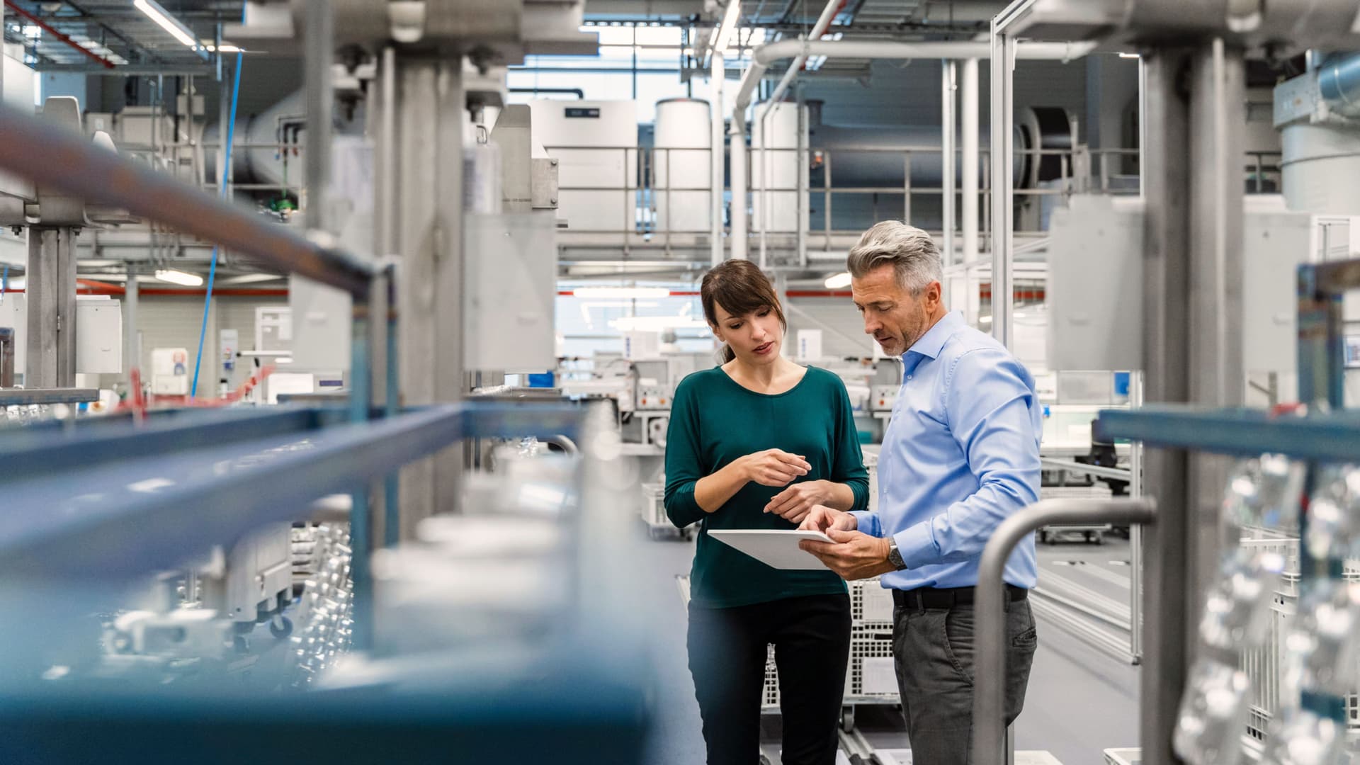 Eine Frau bespricht sich mit einem Kollegen in einer modernen Industrieanlage. Sie schauen beide auf ein Tablet.