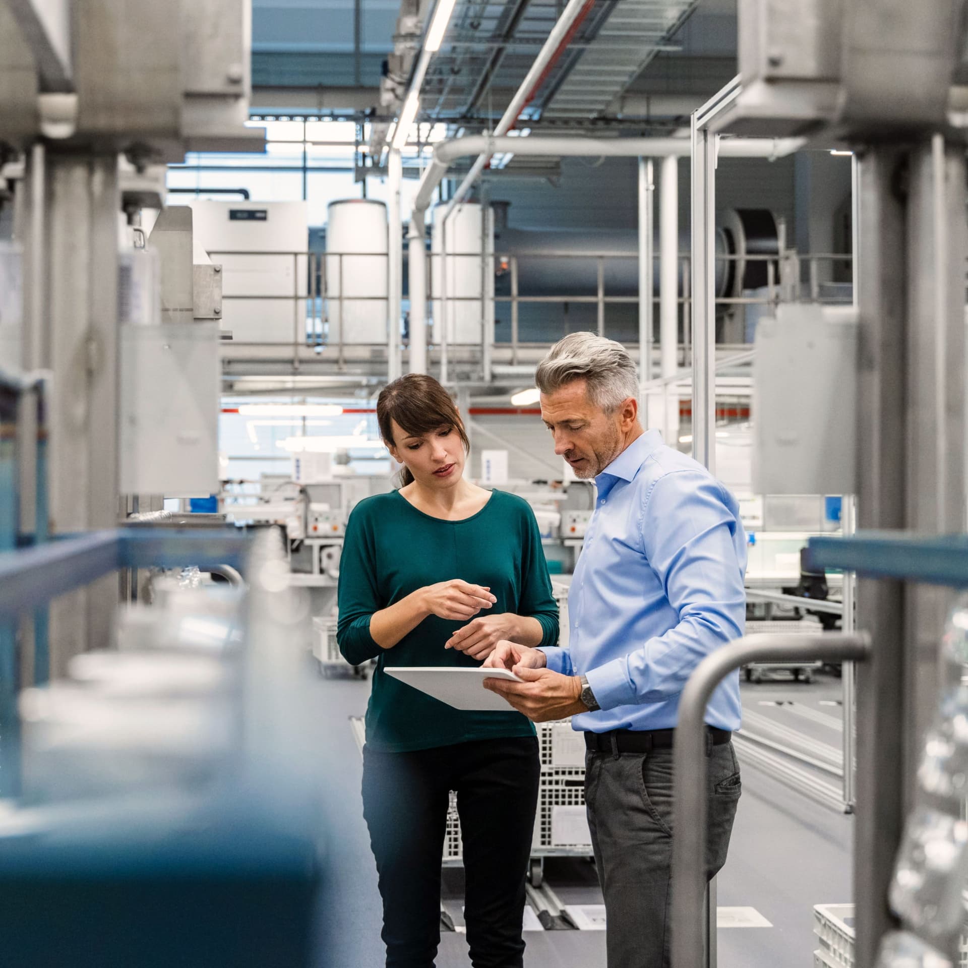 Eine Frau bespricht sich mit einem Kollegen in einer modernen Industrieanlage. Sie schauen beide auf ein Tablet.