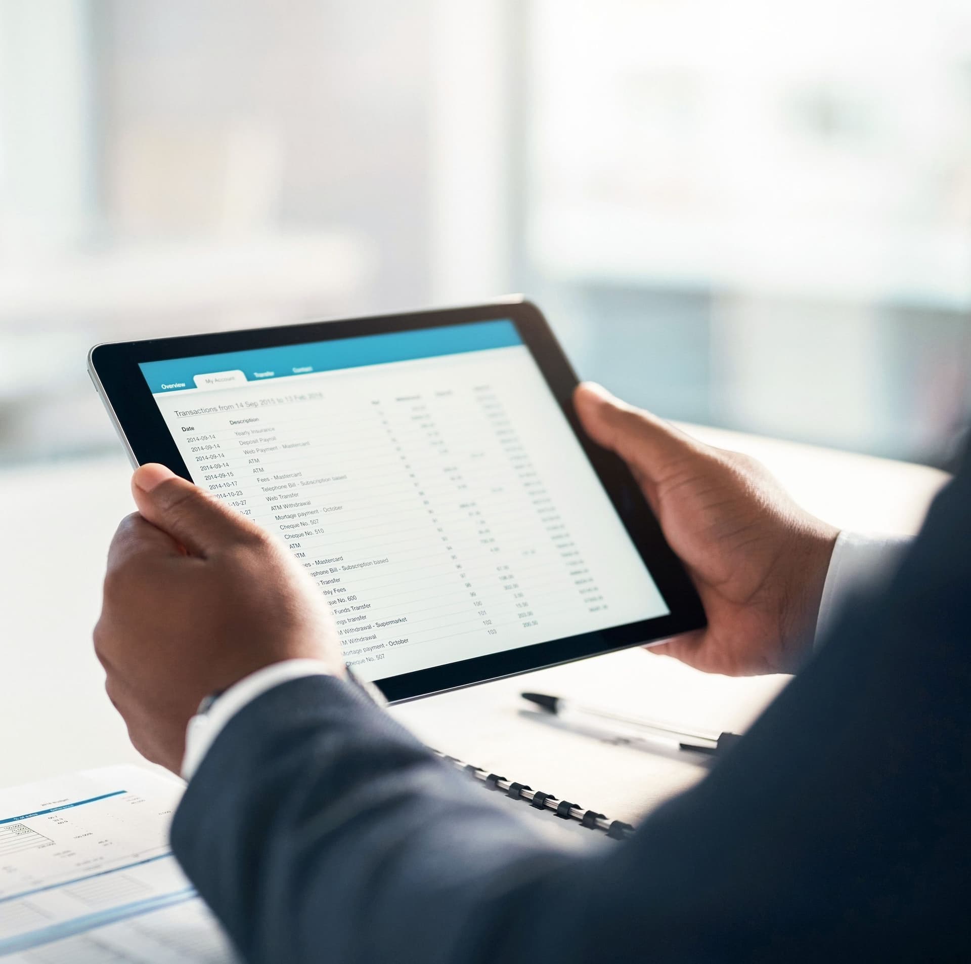 Blick über die Schulter einer Person in Anzug auf einen Tablet-Computer in deren Händen