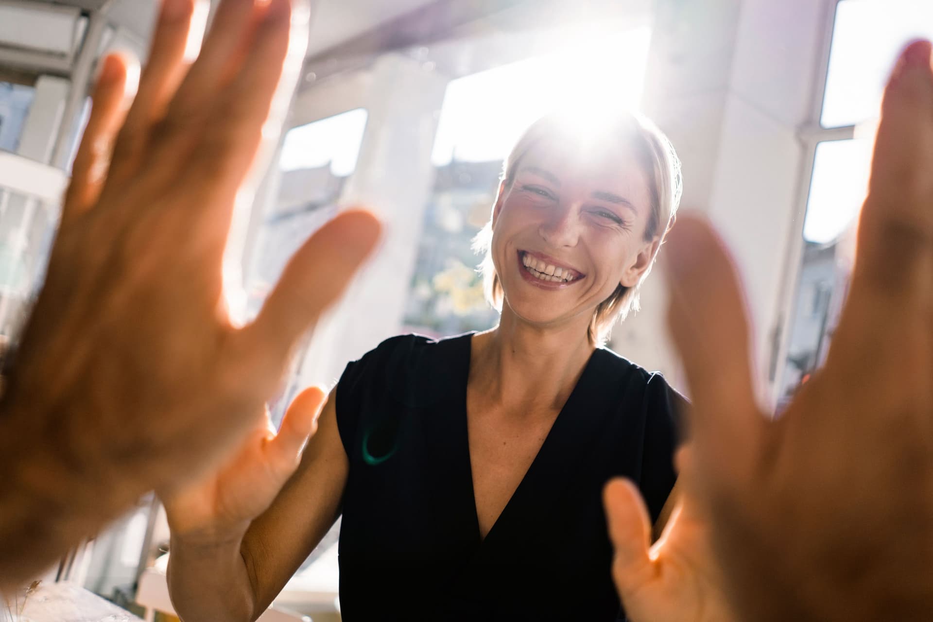 Lachende Frau gibt einem Kollegen High Five und guckt dabei in die Kamera. 