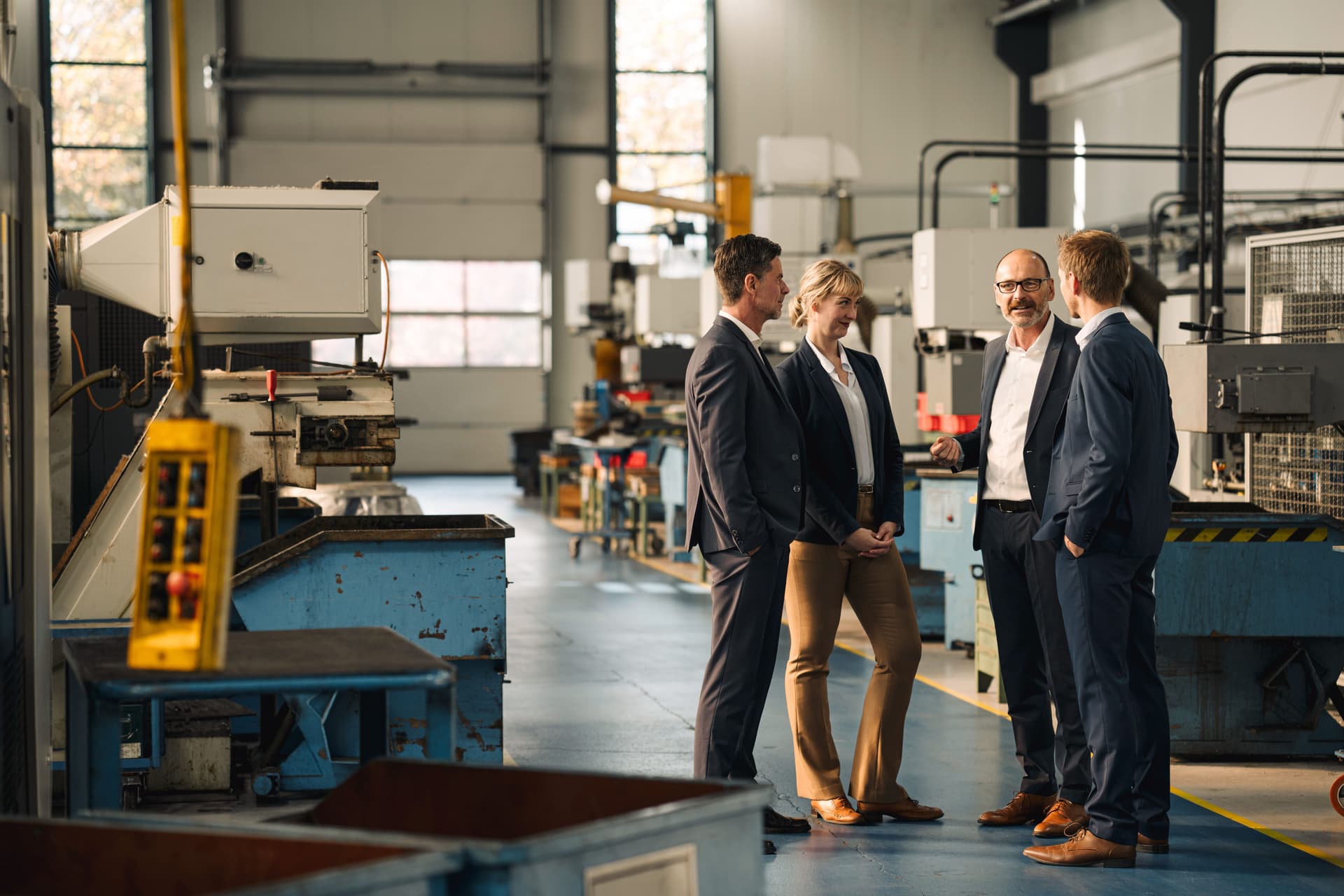 Eine Frau und drei Männer stehen zusammen bei einem Meeting in einer Fabrik.