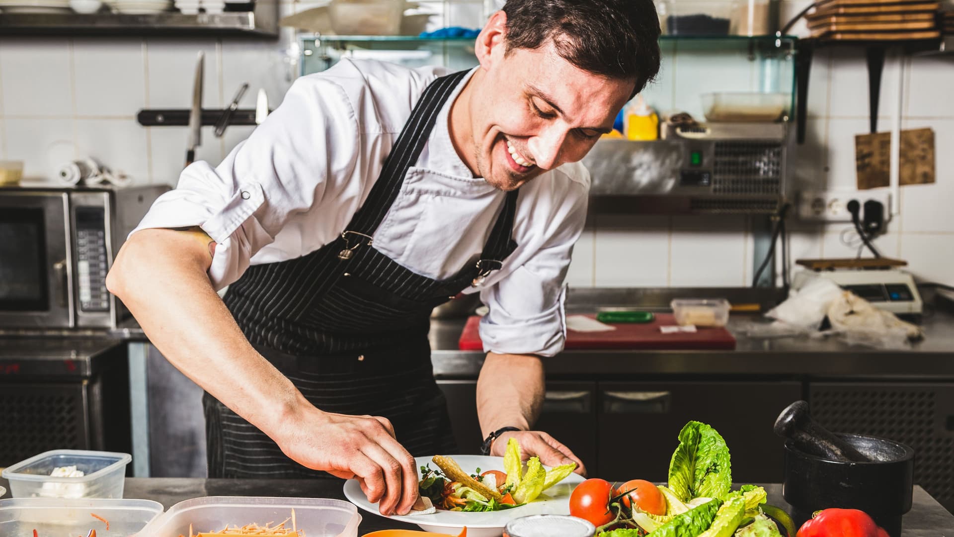 Professioneller Koch richtet lächelnd einen Salat in einer Restaurantküche an.