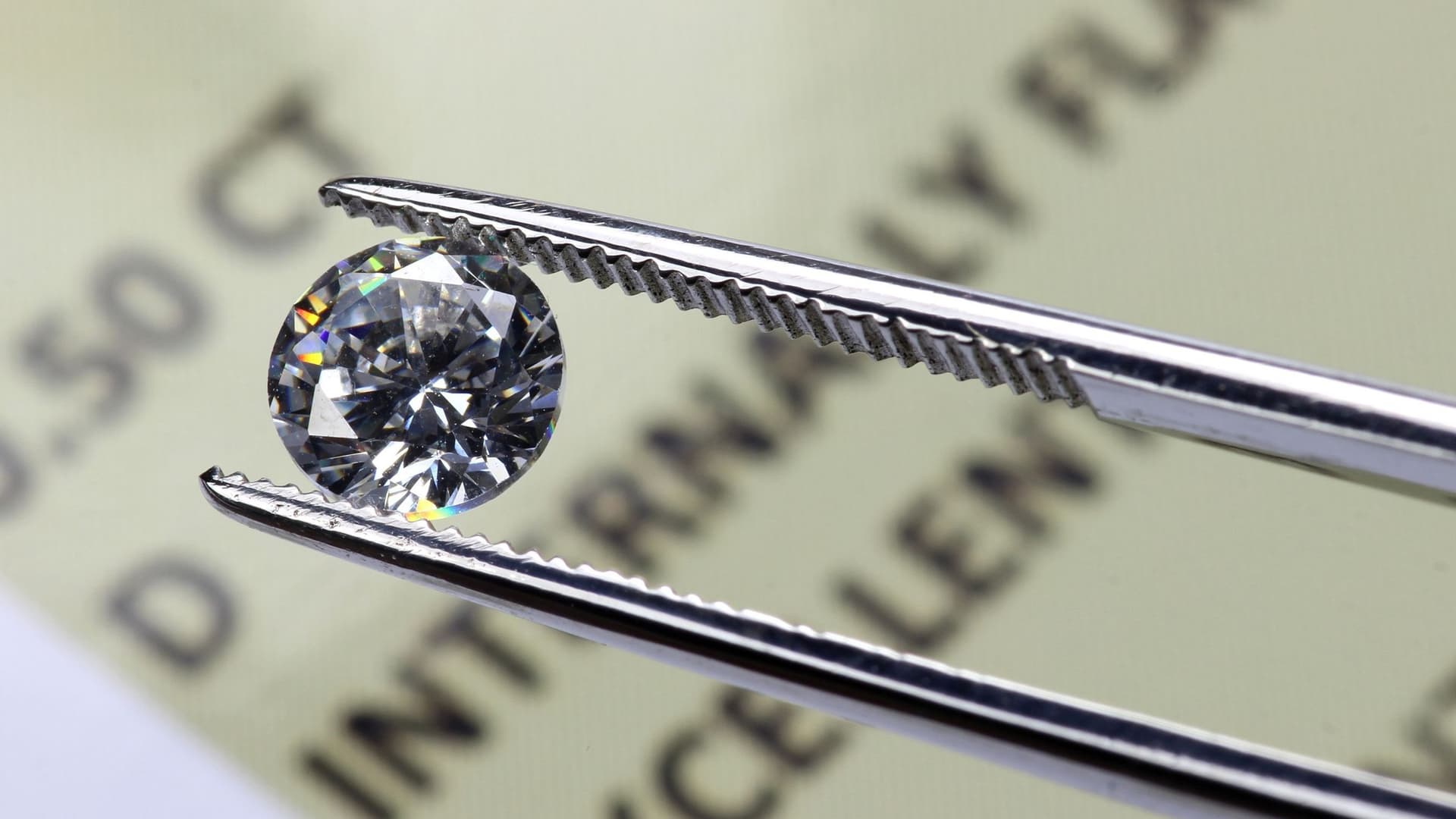 Pinzette hält einen Diamanten. Darunter liegt ein Papier mit Text.
