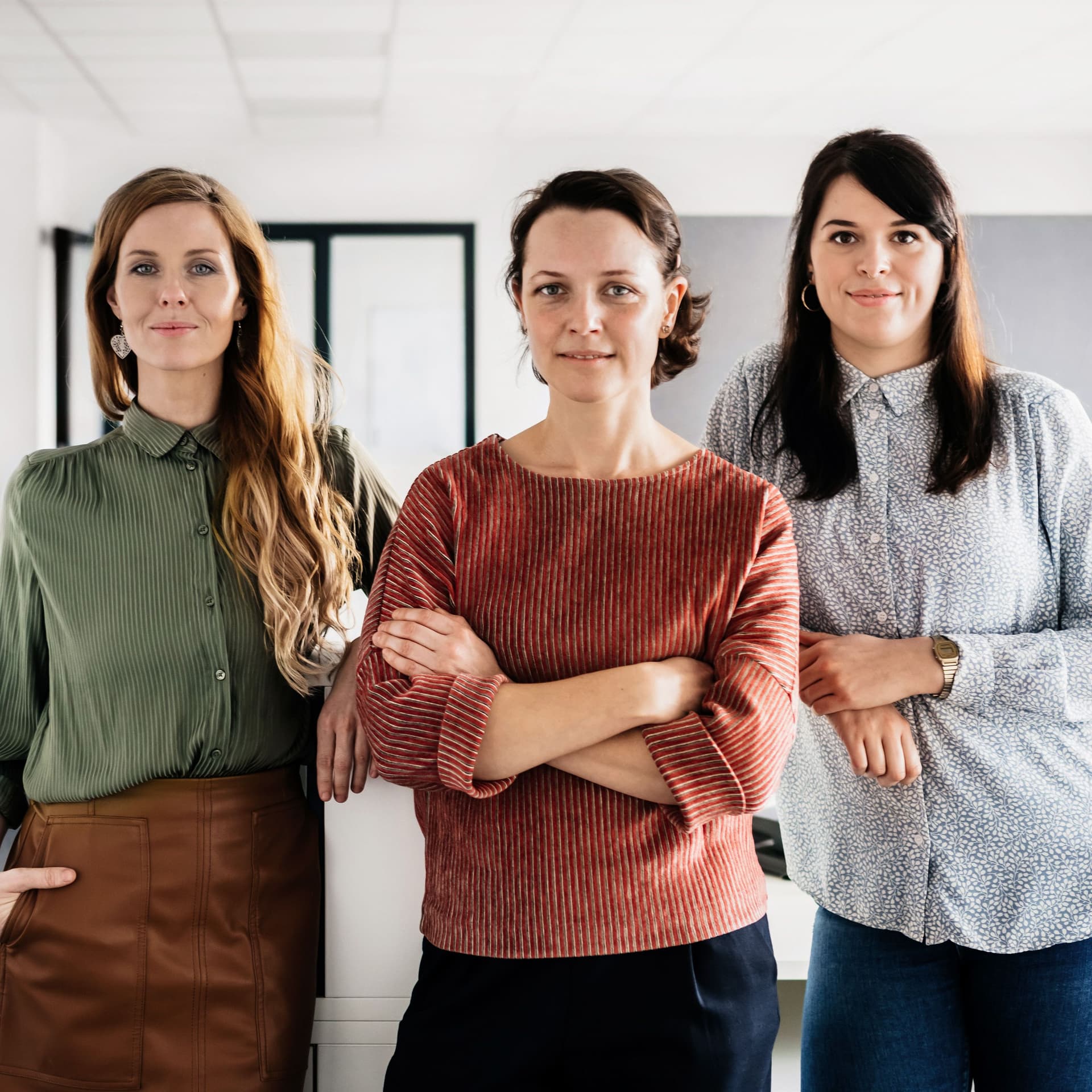 Drei Frauen stehen in einem Büro. Im Hintergrund sind Computer.