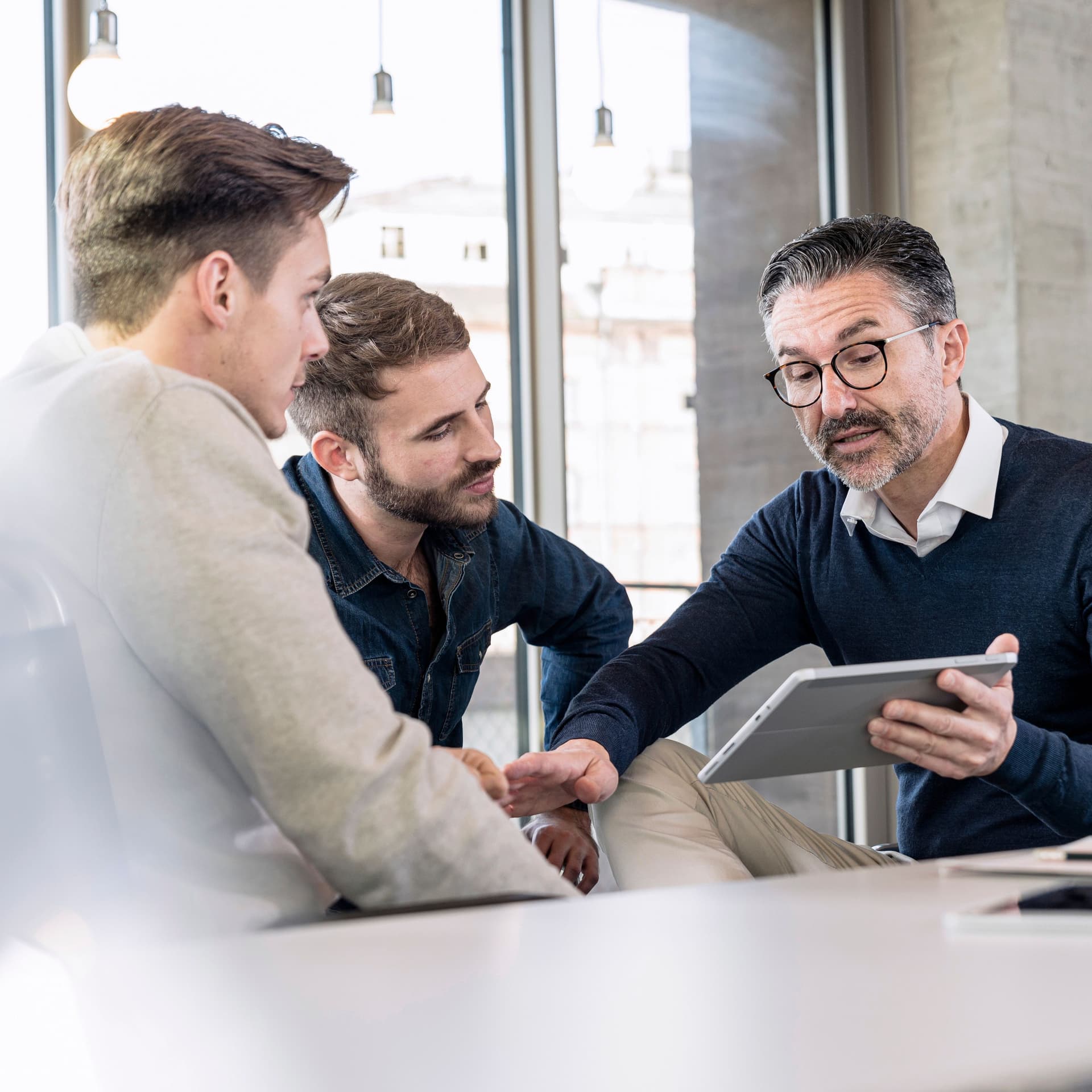 Drei Geschäftsmänner sitzen zusammen in einem Büro und gucken auf ein Tablet.