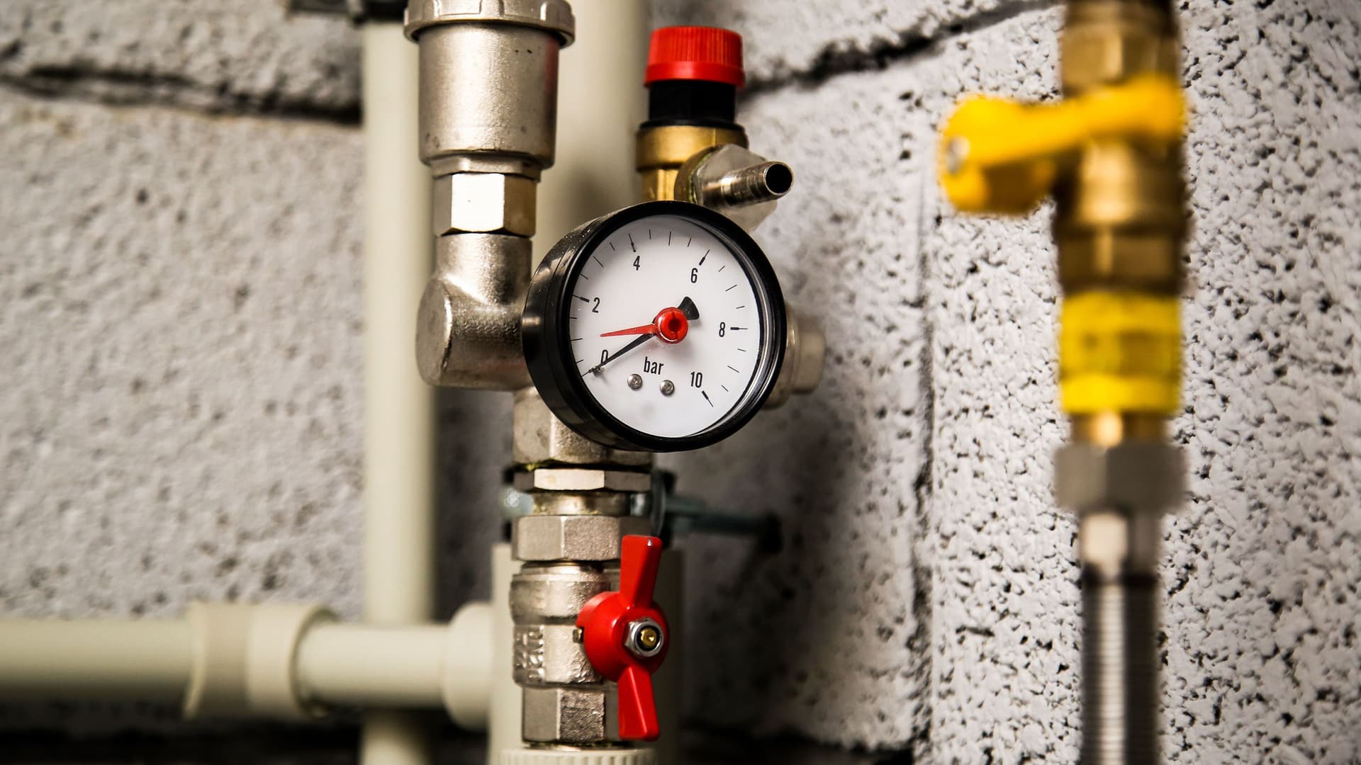 Nahaufnahme von Manometer, Rohren und Hahnventilen der Heizungsanlage in einem Heizraum