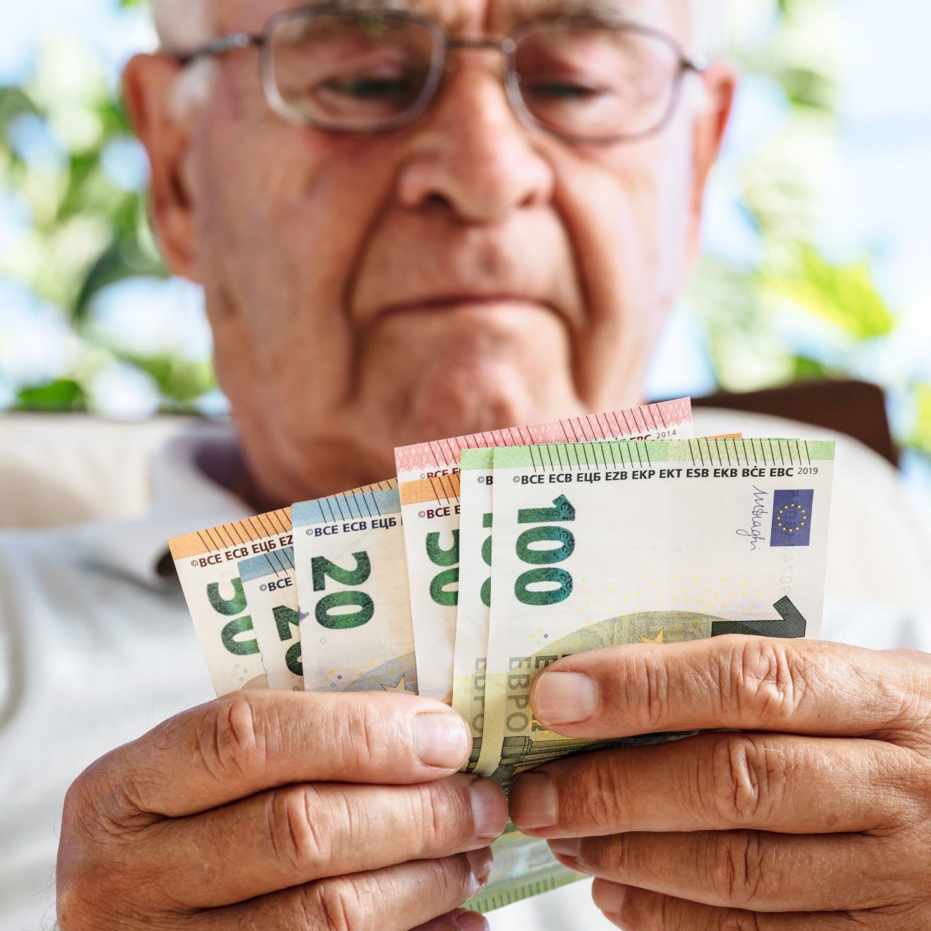 Ein älterer Mann schaut auf ein Bündel Geldscheine in der Hand.