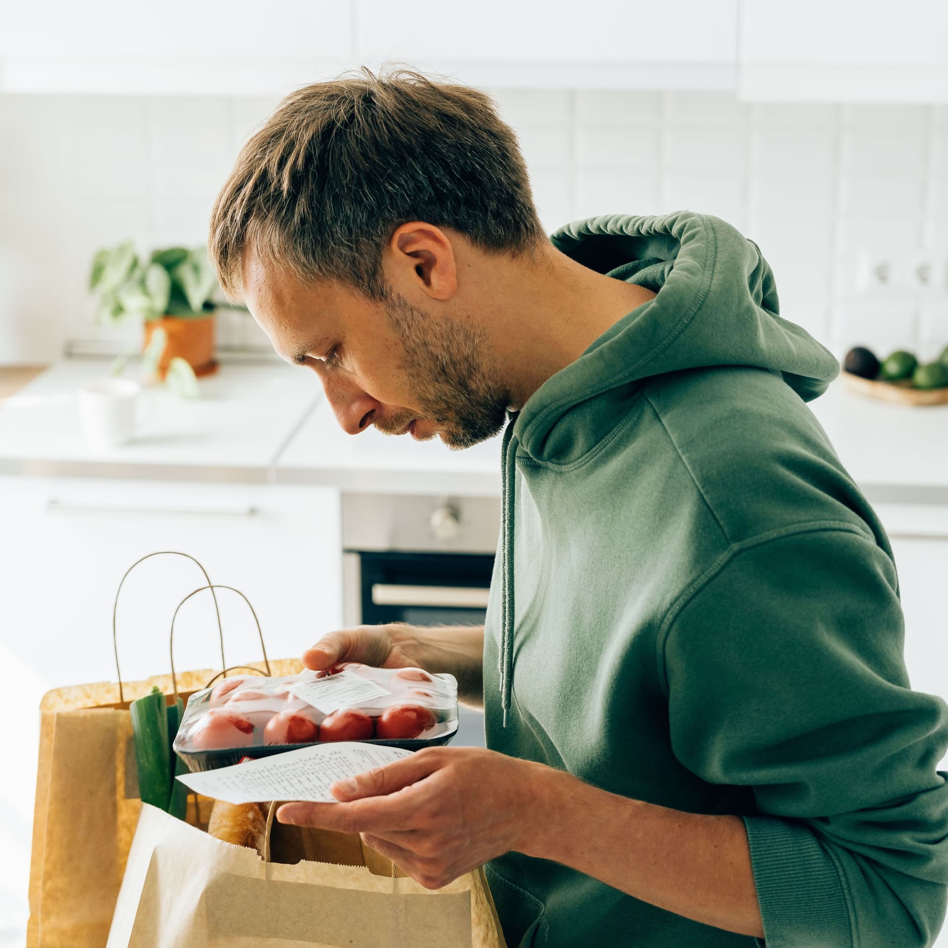 Ein Mann in grünem Hoodie schaut in seiner Einkaufstüte. Er hat einen Zettel in der Hand.