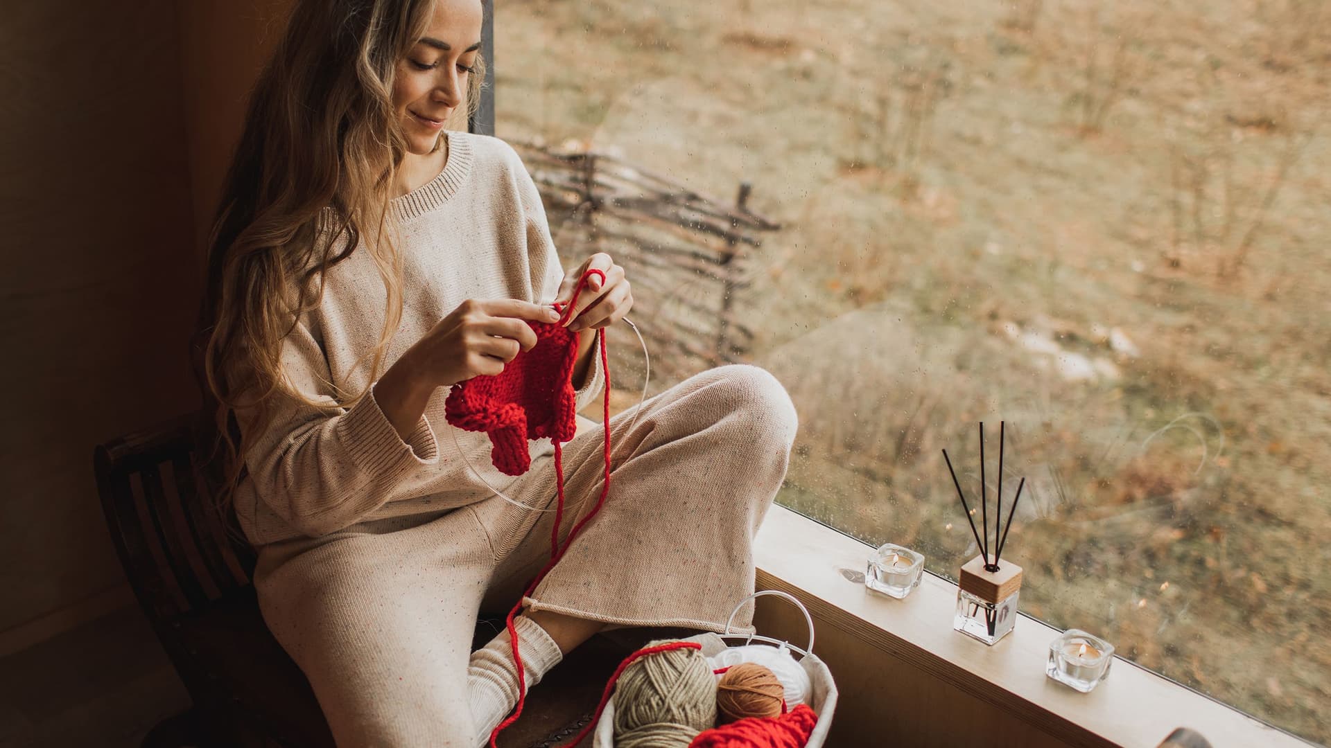 Eine junge Frau sitzt am Fenster und strickt.