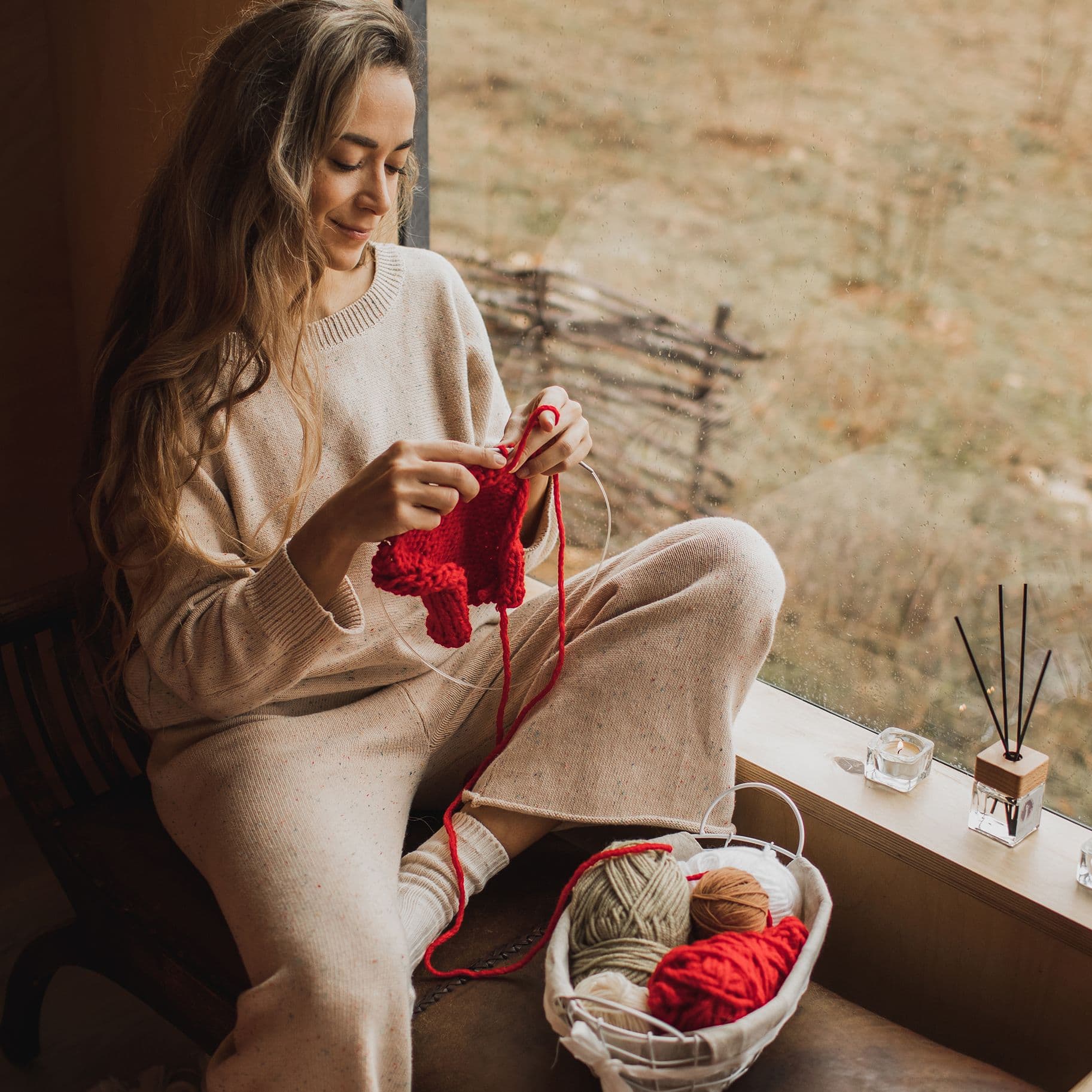 Eine junge Frau sitzt am Fenster und strickt.