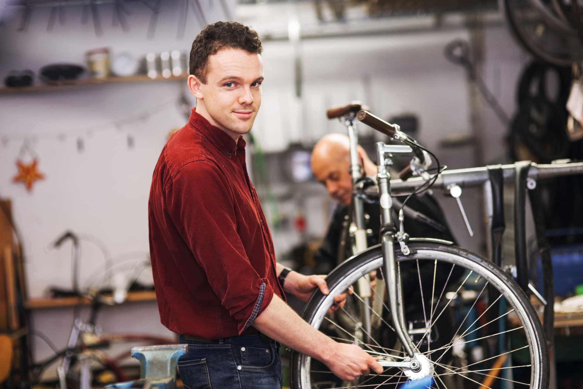 Ein junger Fahrradtechniker, der in einer Werkstatt an dem Vorderrad eines Fahrrads arbeitet und in die Kamera lächelt.
