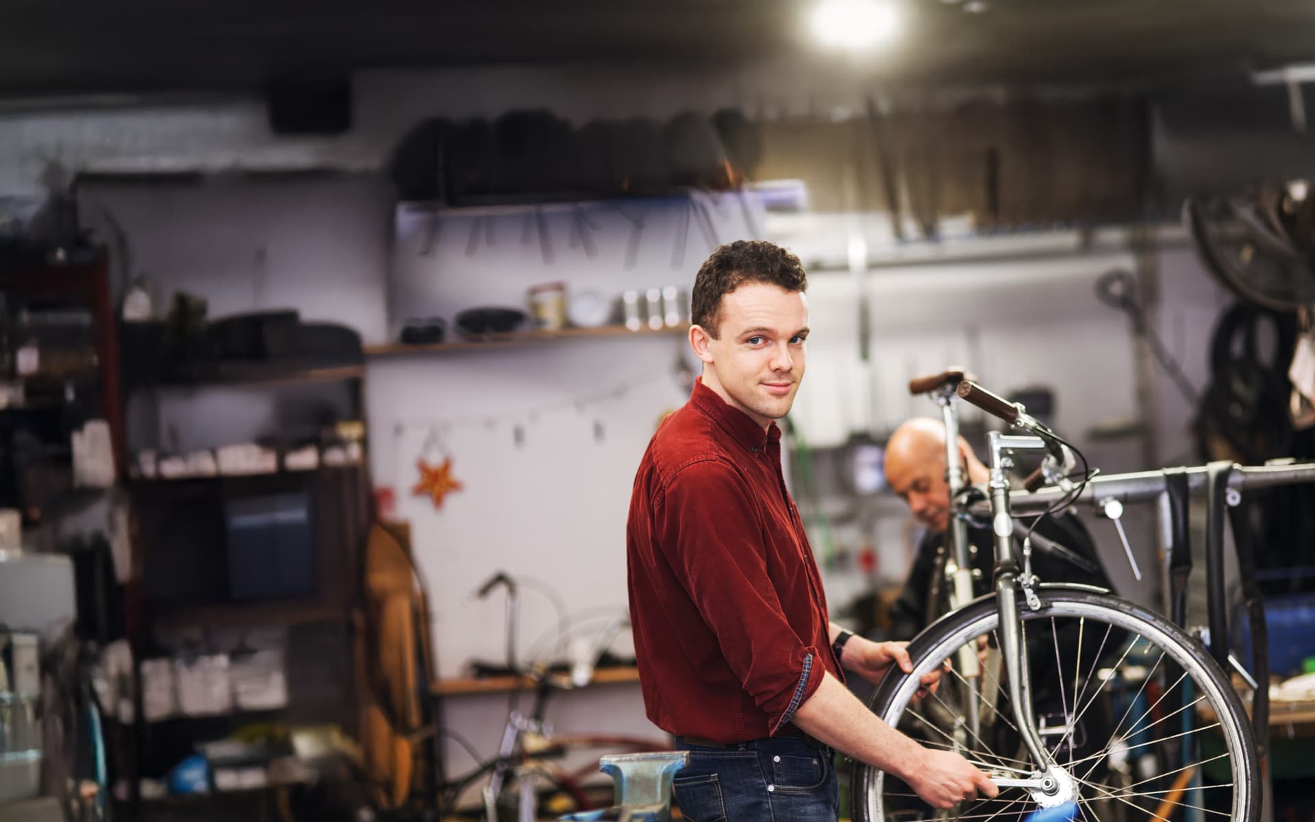 Ein junger Fahrradtechniker, der in einer Werkstatt an dem Vorderrad eines Fahrrads arbeitet und in die Kamera lächelt.