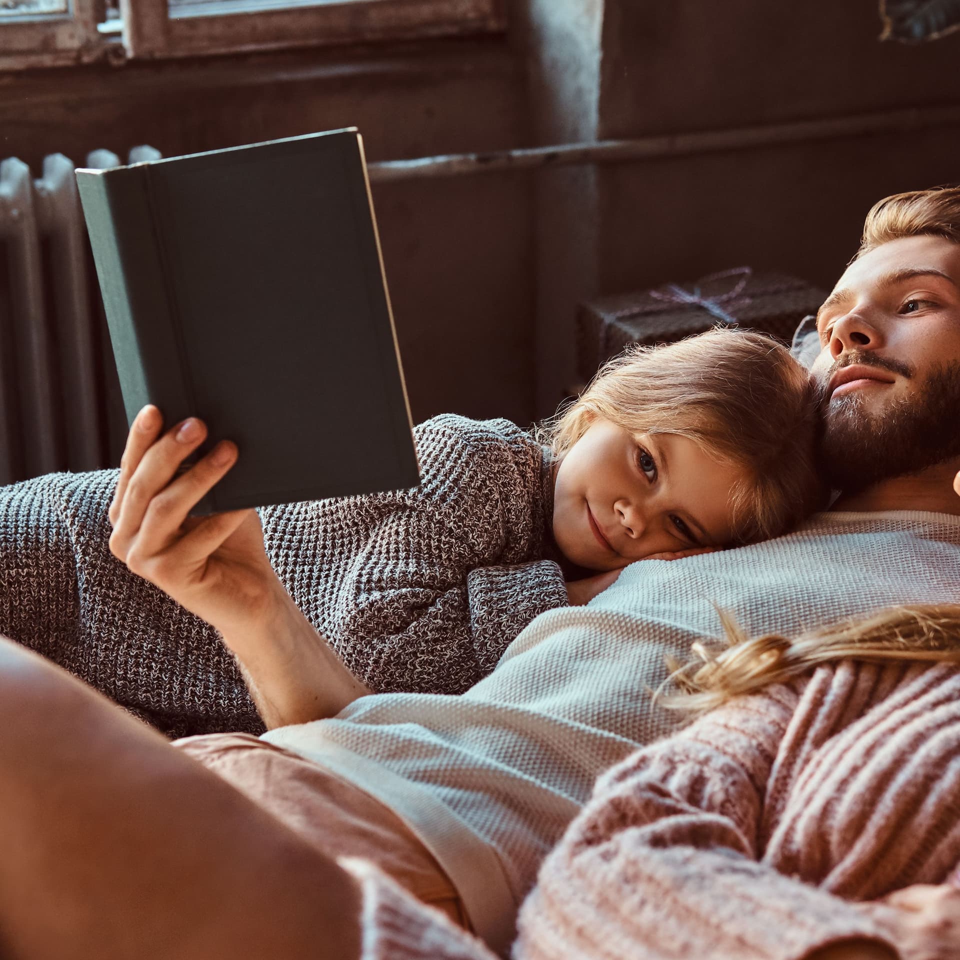 Frau, Mann und Kind lesen liegend gemeinsam ein Buch.