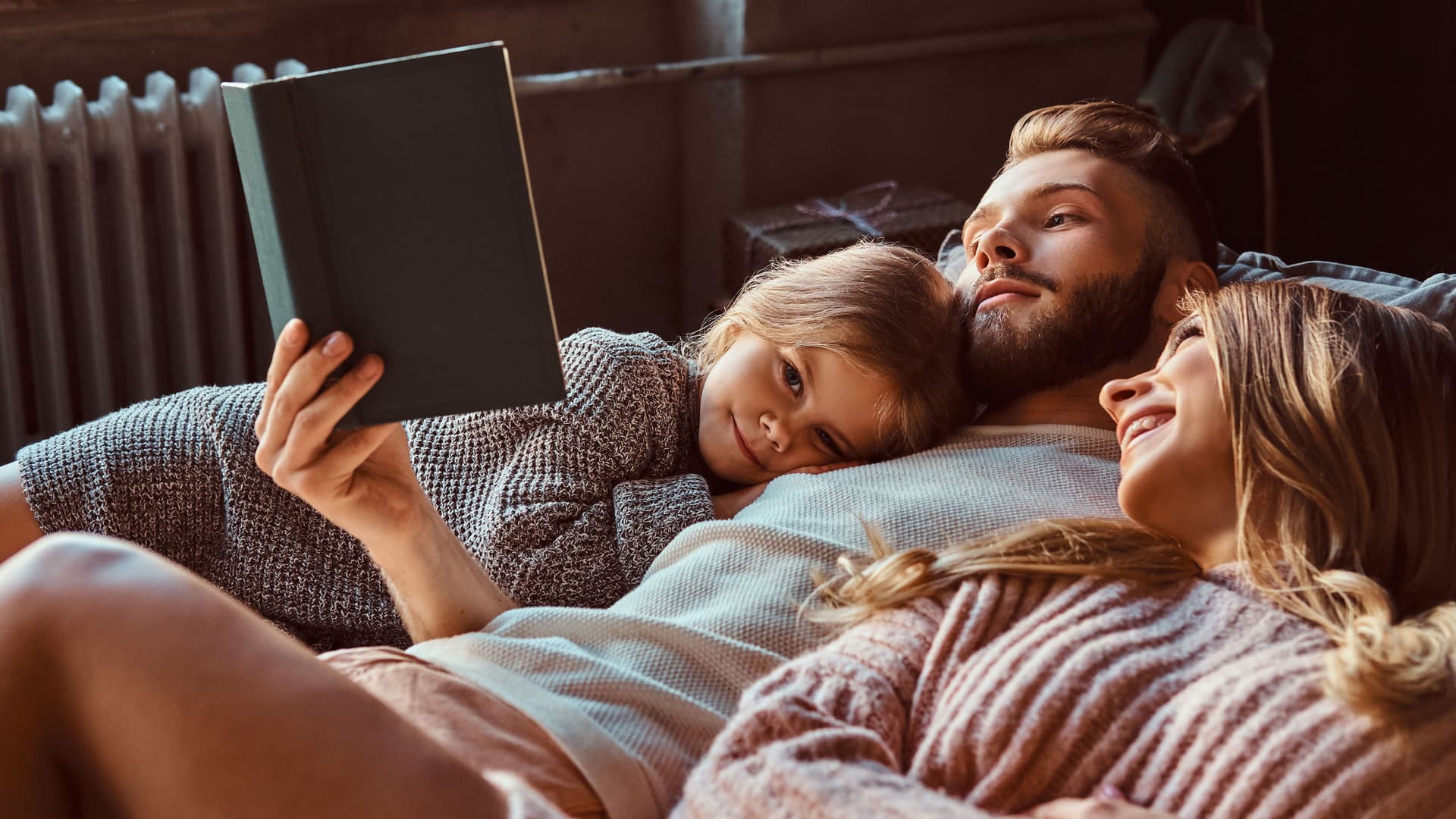 Frau, Mann und Kind lesen liegend gemeinsam ein Buch.