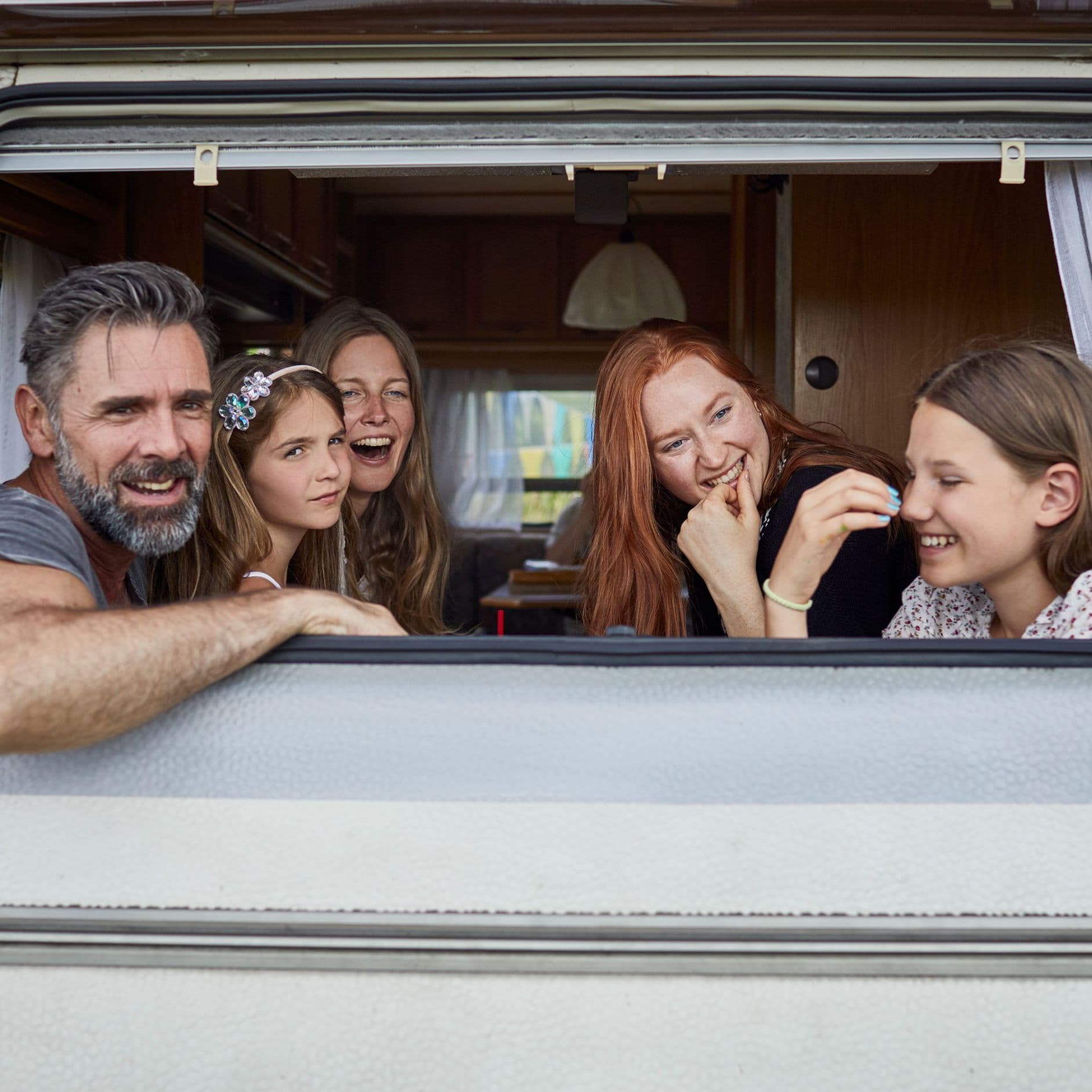 Eine Familie schaut aus dem Heckfenster eines Wohnmobils. Sie lachen.