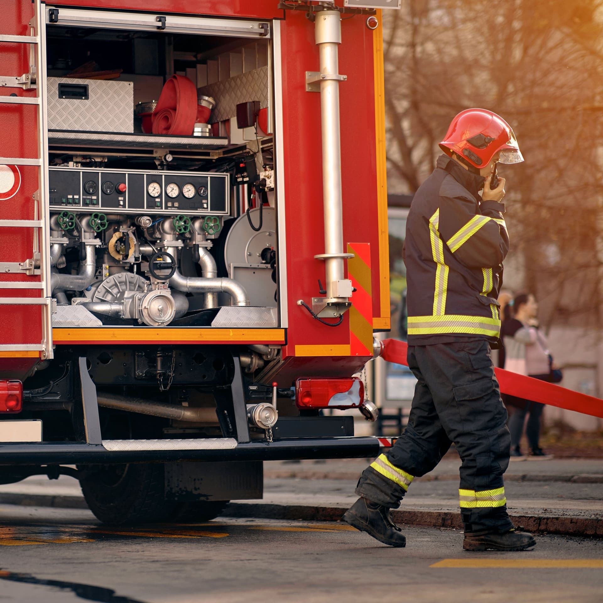 Rotes Feuerwehrfahrzeug mit Feuerwehrmann im Vordergrund im Einsatz.
