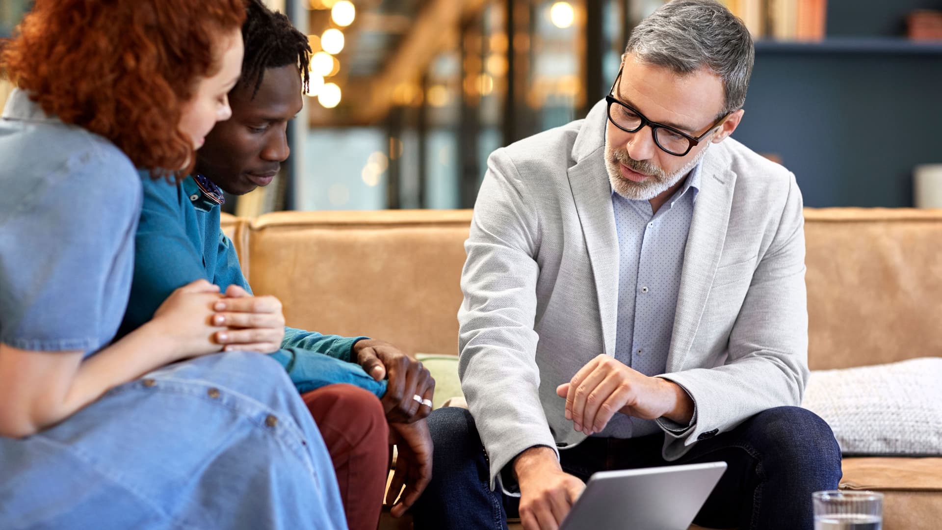 Finanzberaterplanung mit jungem multiethnischem Paar im Büro. Der Geschäftsmann diskutiert über ein digitales Tablet mit Kunden am Arbeitsplatz. Sie sitzen in Besprechung.